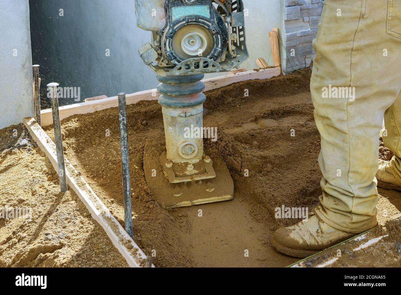 Worker with vibratory plate compactor compacting sand construction new