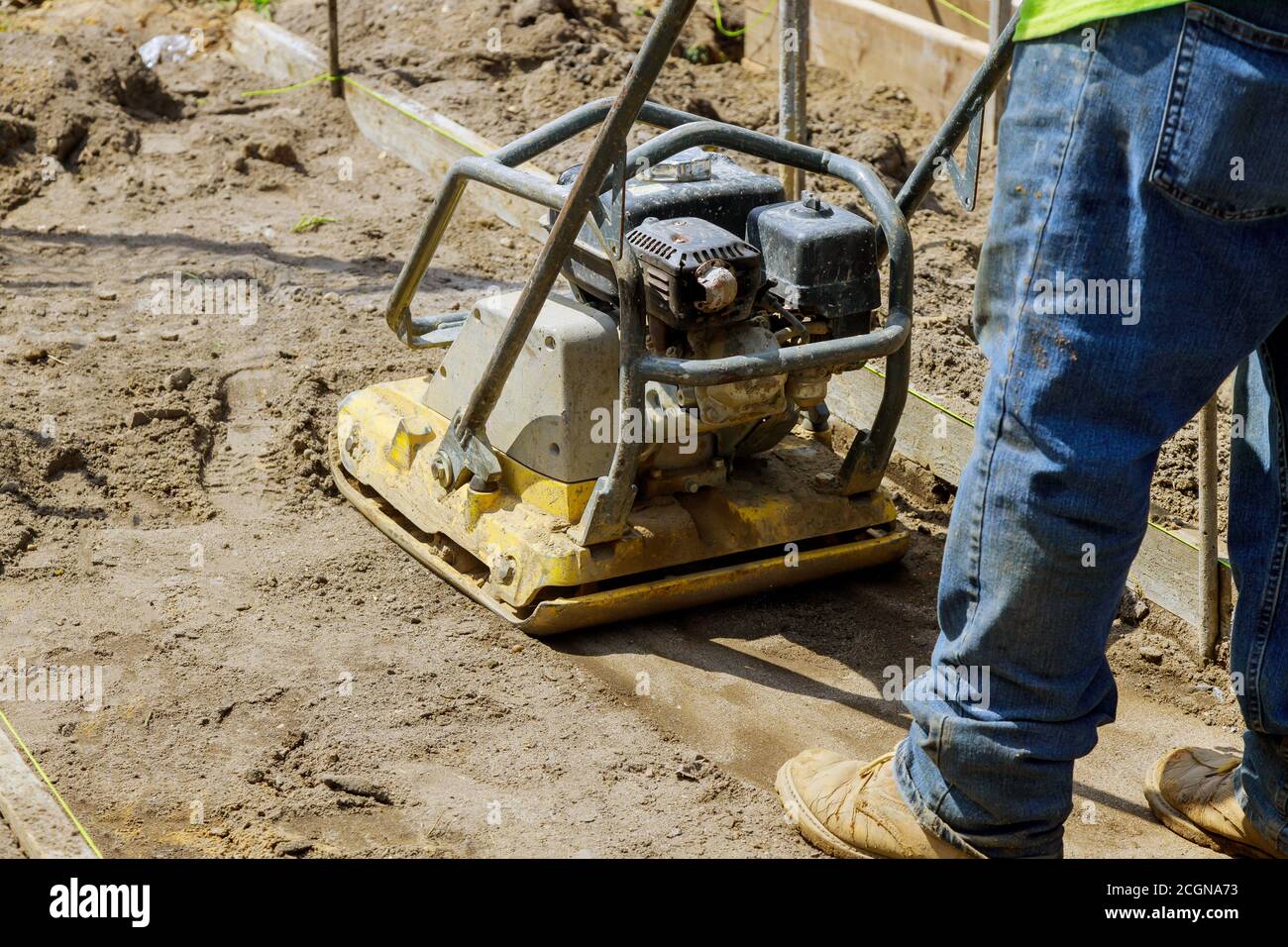 Worker use vibratory plate compactor under construction at soil on new