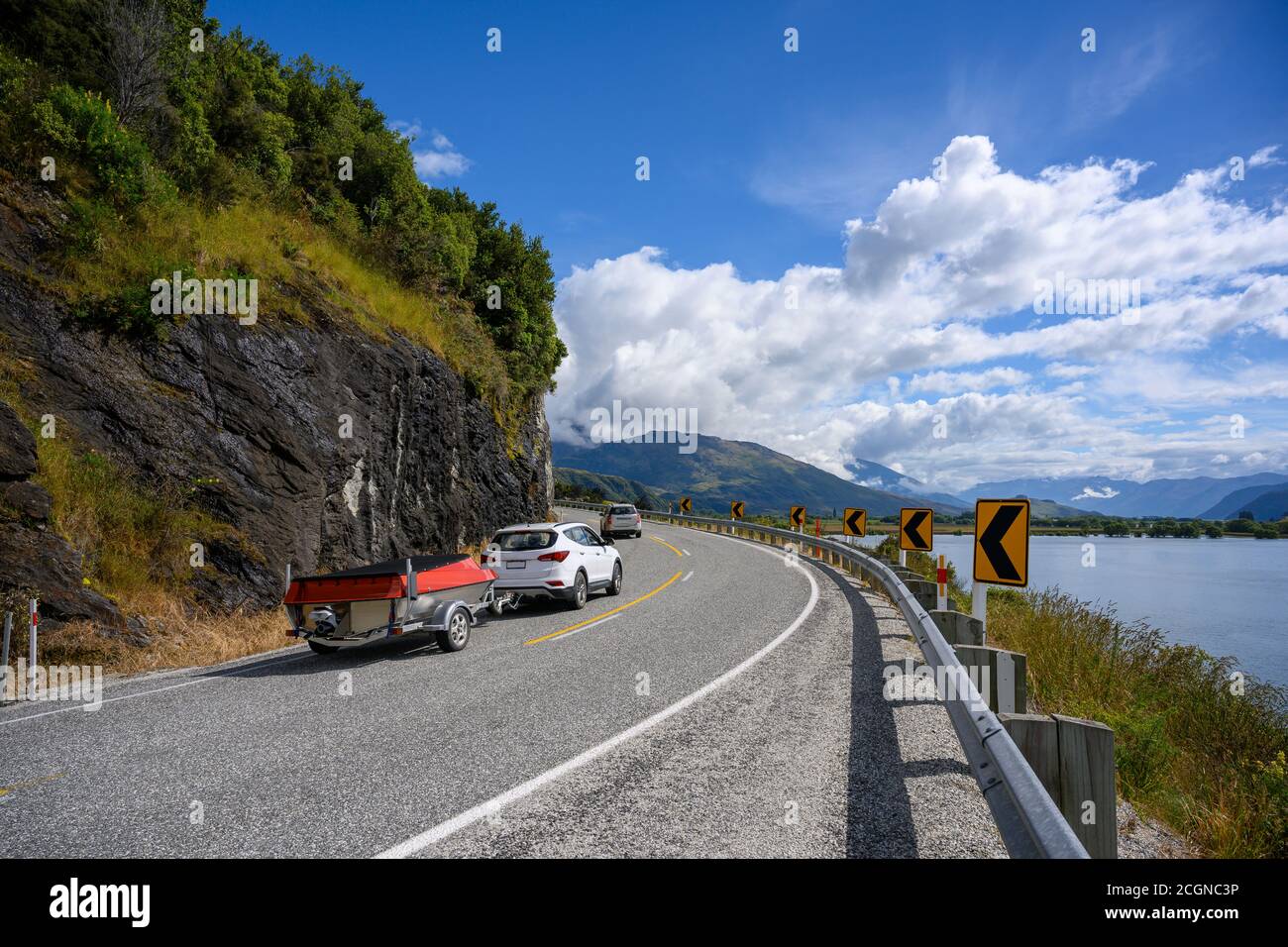 A white car with a boat Running on a curved road up the hill in the summer in wanaka lake, Tourists enjoy driving holiday trips on the South Island of Stock Photo