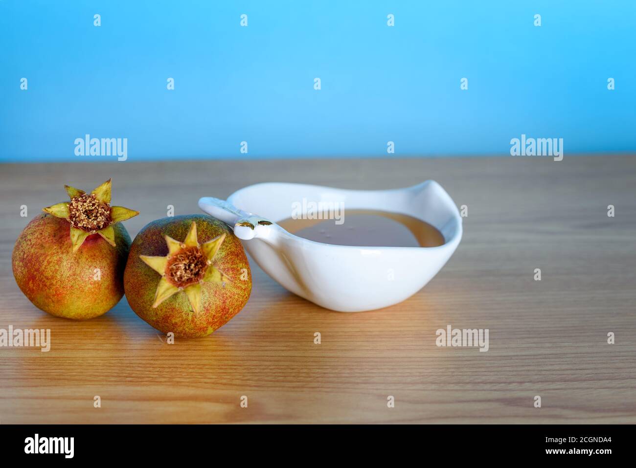 Rosh Ha Shana - Jewish new year composition of pomegranate and white bowl of honey for Rosh Hashanah on wooden table over blue background.Greeting card with copy space. Stock Photo