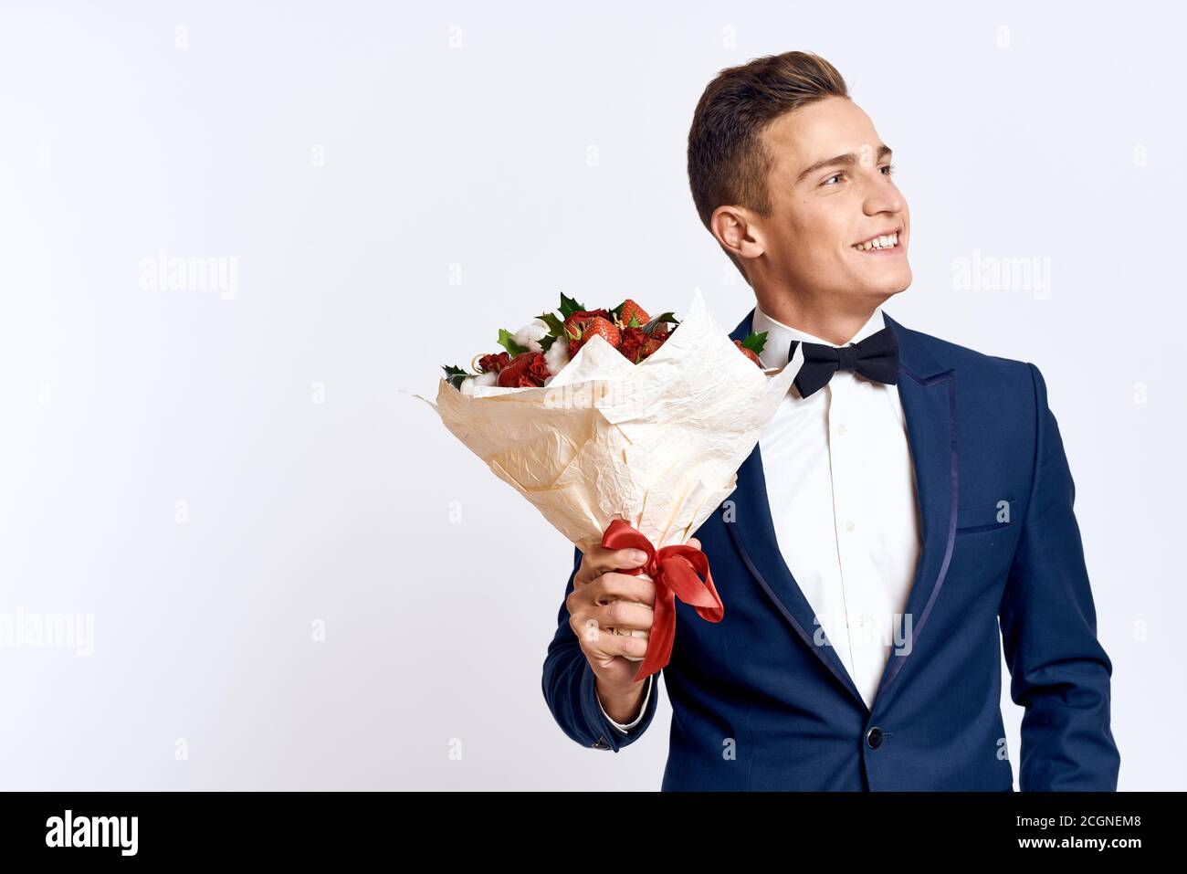 An elegant man in a classic suit with a bow tie holds a bouquet of ...