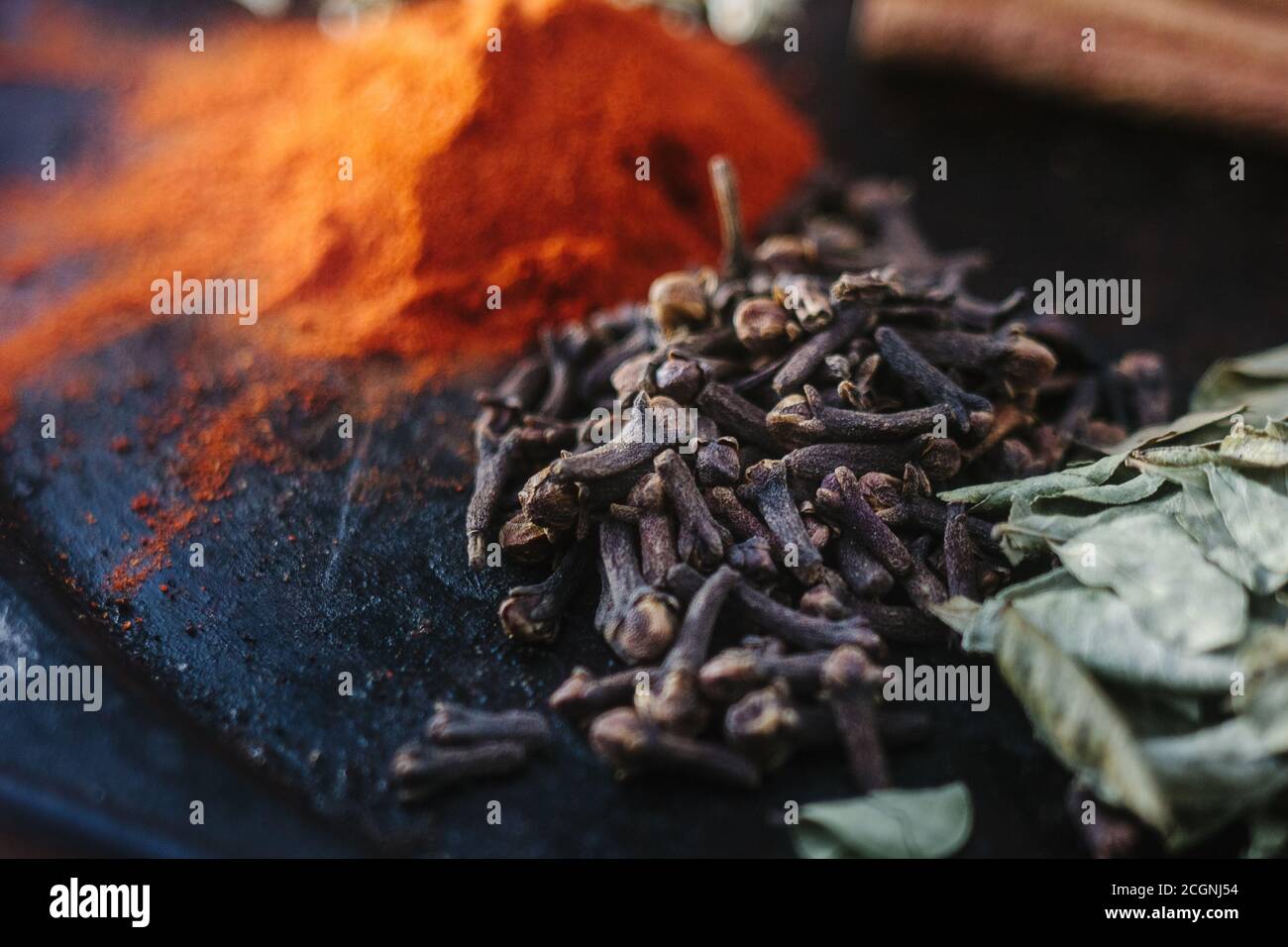 Black cloves spice over black plate surrounded by spices Stock Photo