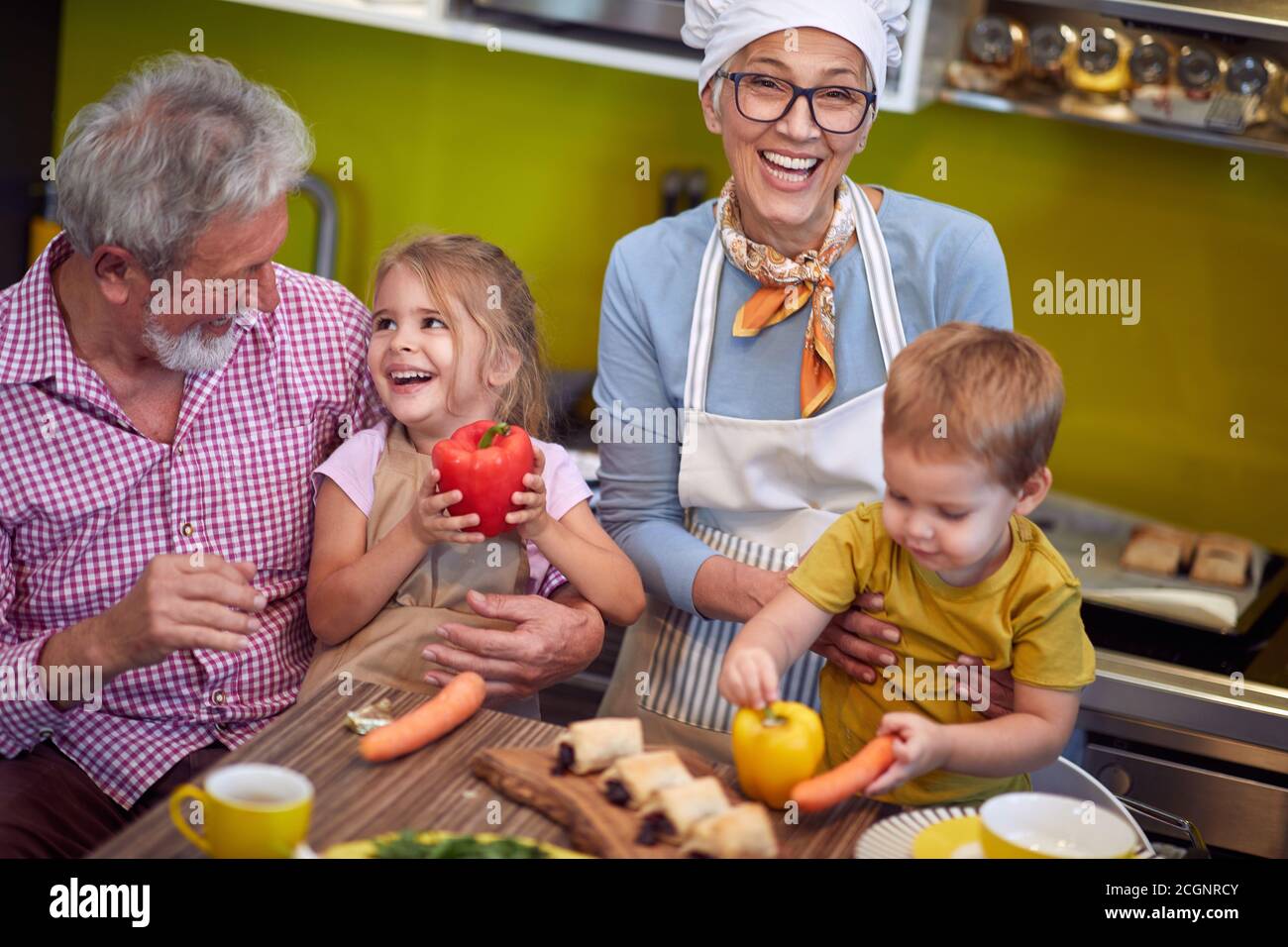 top view of grandparents enjoying with their grandchildren in the kitchen, laughing Stock Photo