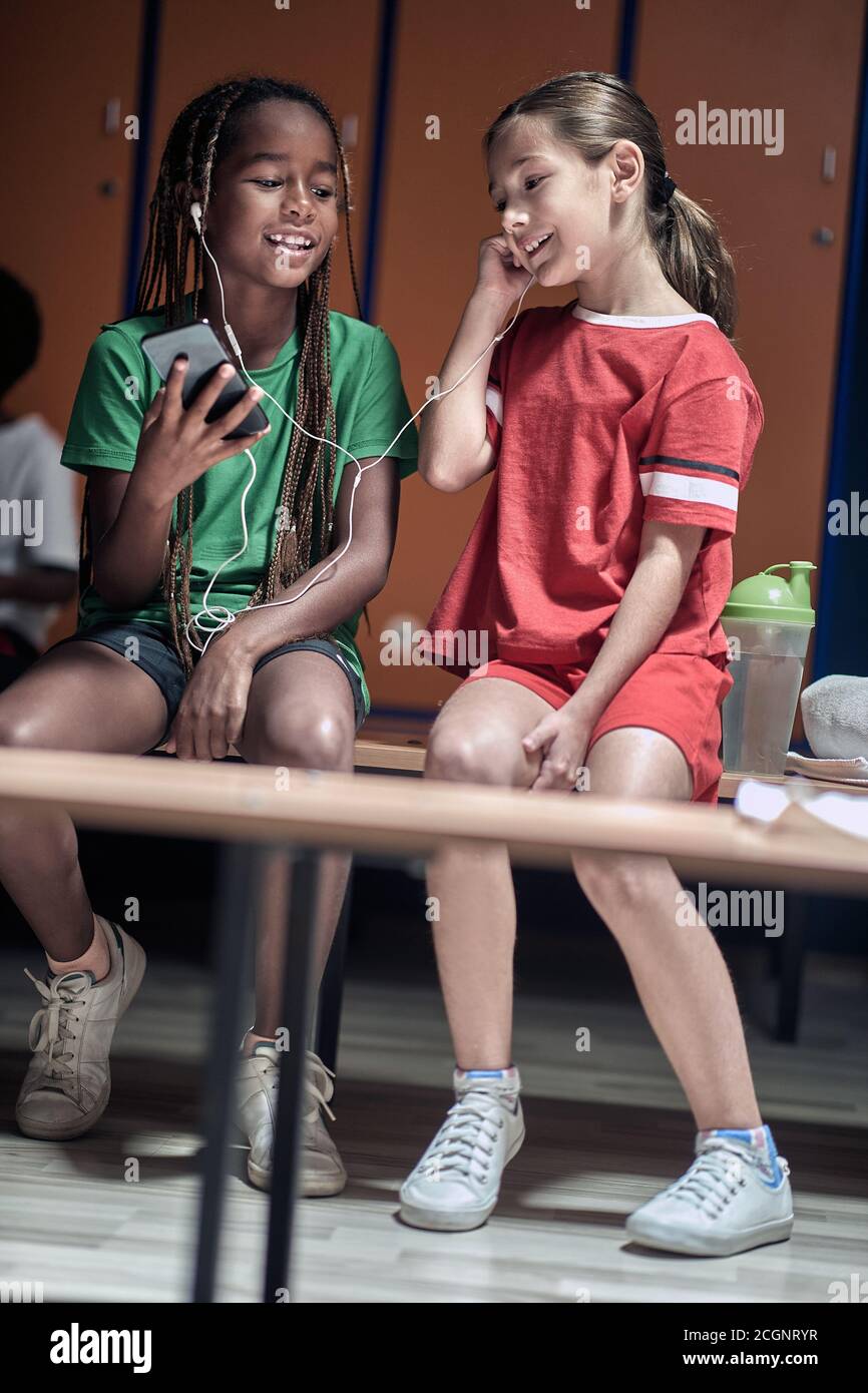 The little soccer teammates enjoying music on cell phone waiting for a training in a locker room Stock Photo