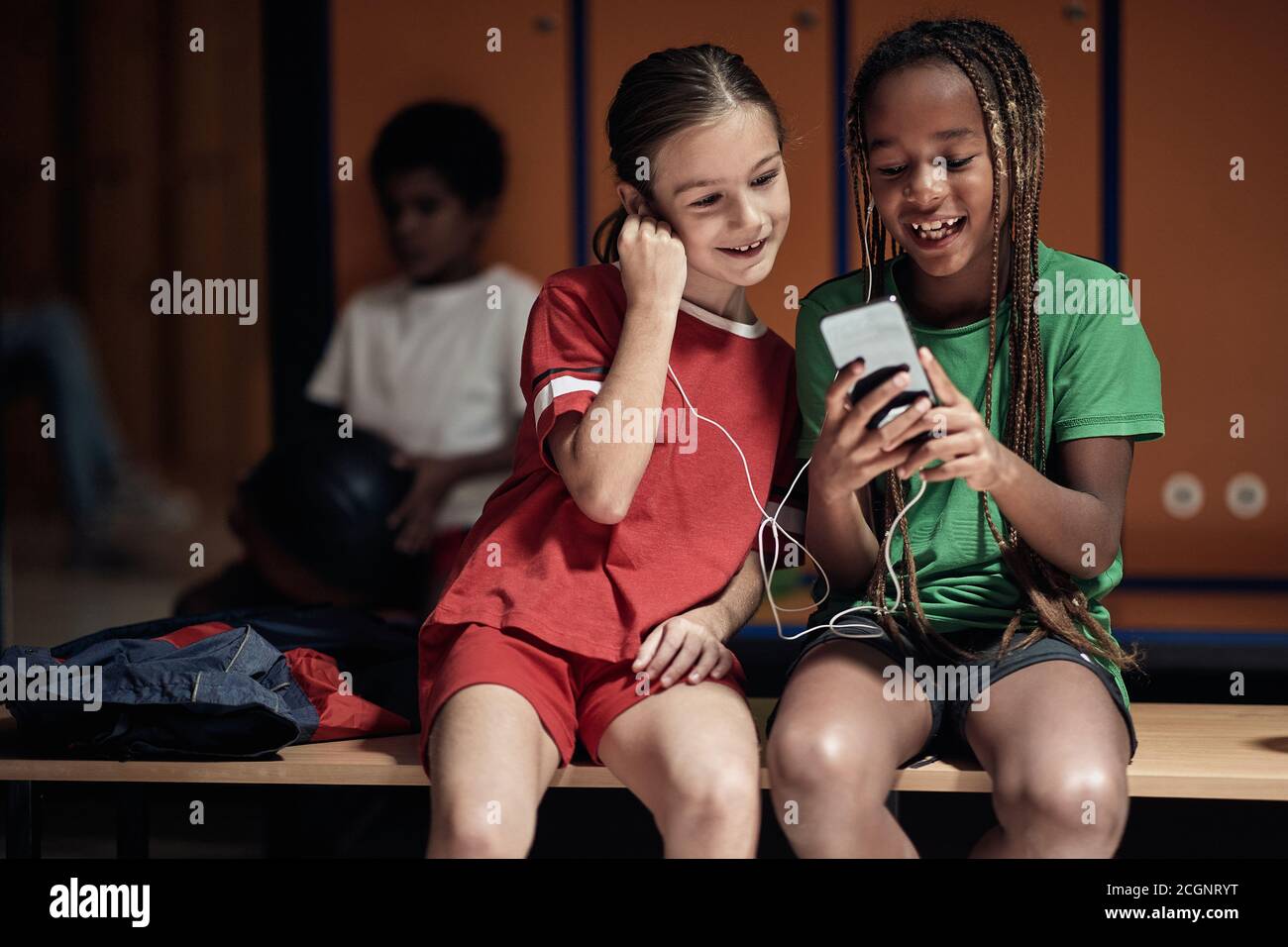 The little soccer teammates enjoying content on cell phone waiting for a training in a locker room Stock Photo
