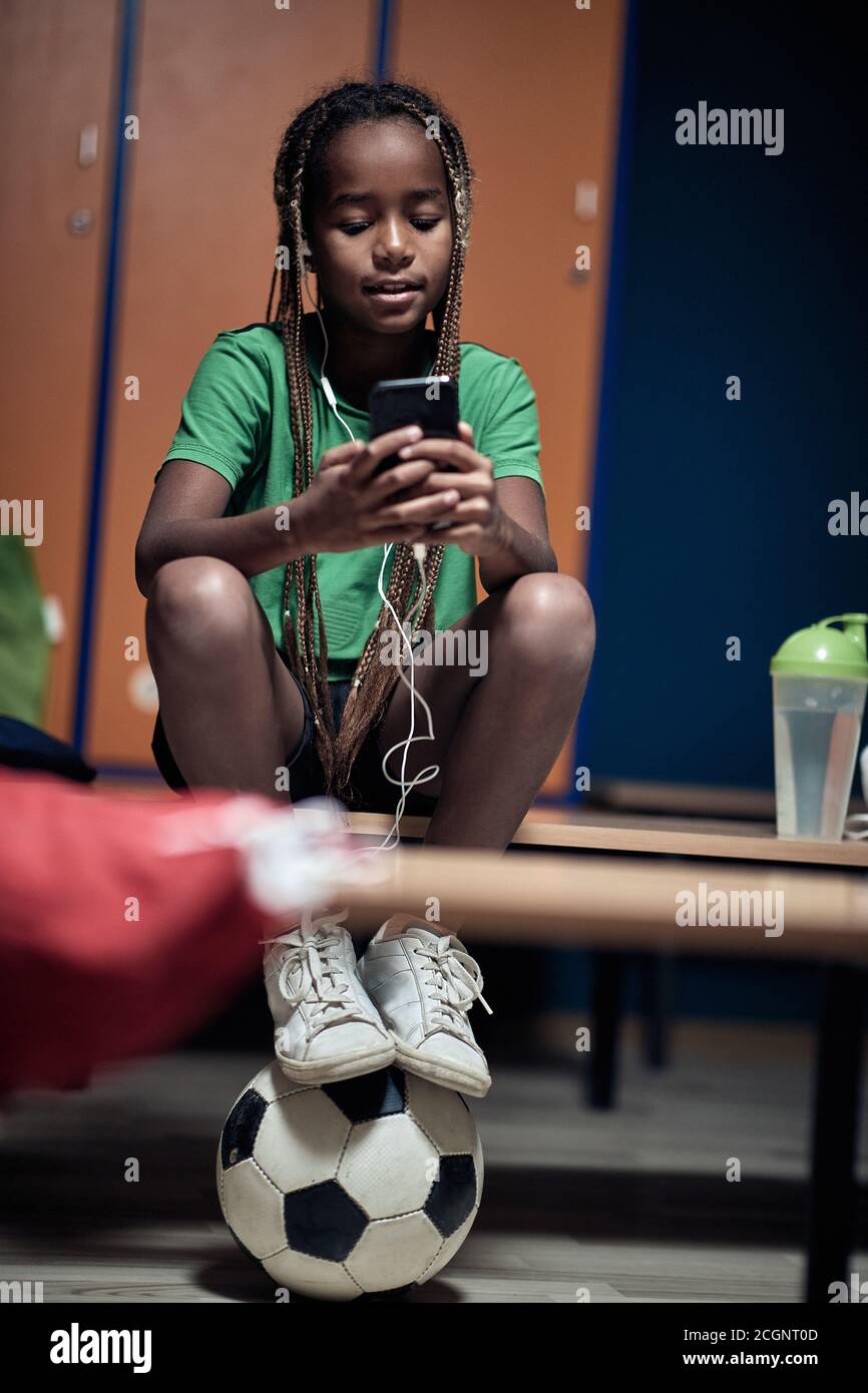 A little soccer player  enjoying music on cell phone waiting for a training  in a locker room Stock Photo