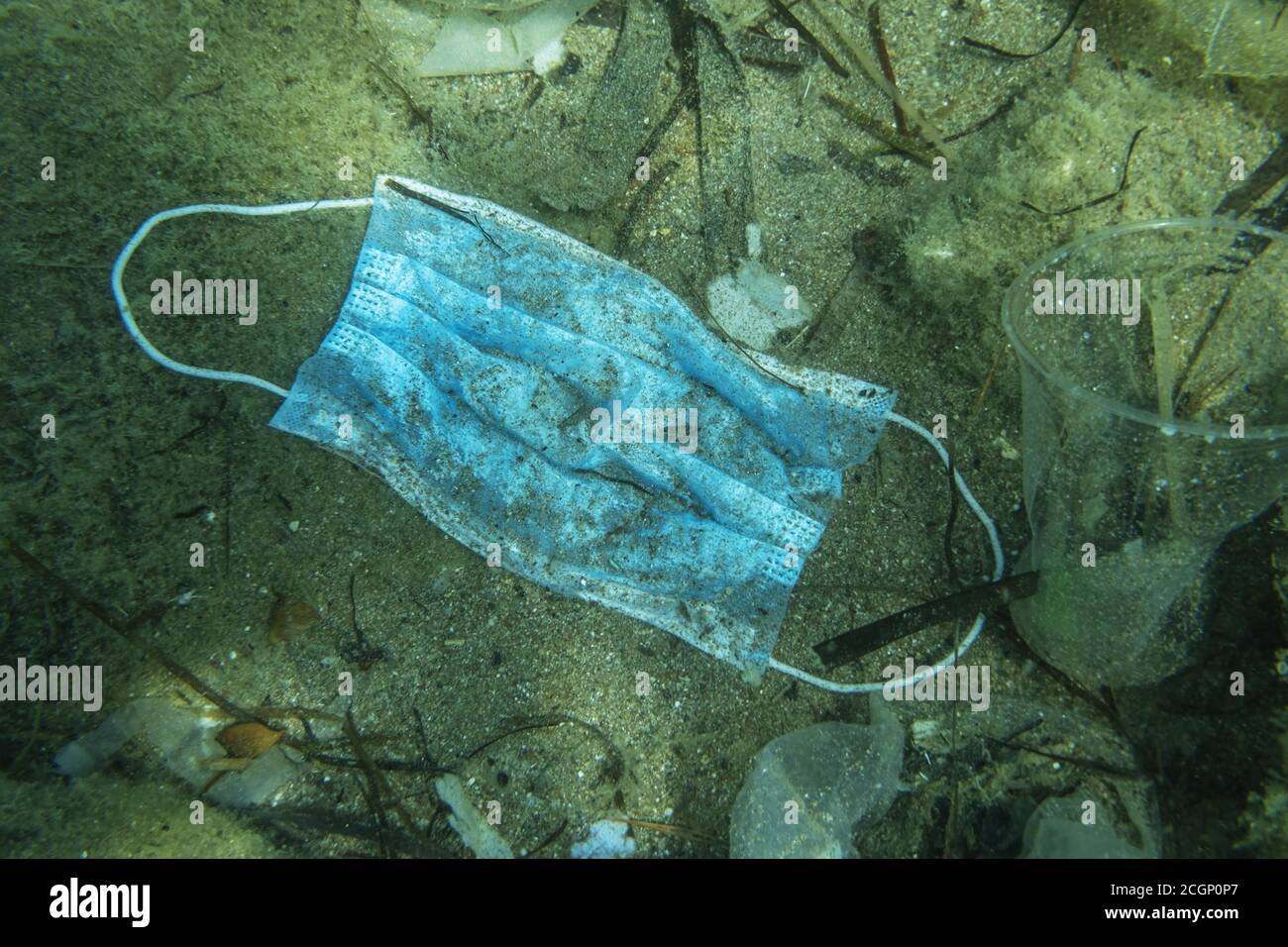 Discarded used medical face mask lies on the seabed together with other plastic waste, Becici, Budva region, Montenegro Stock Photo