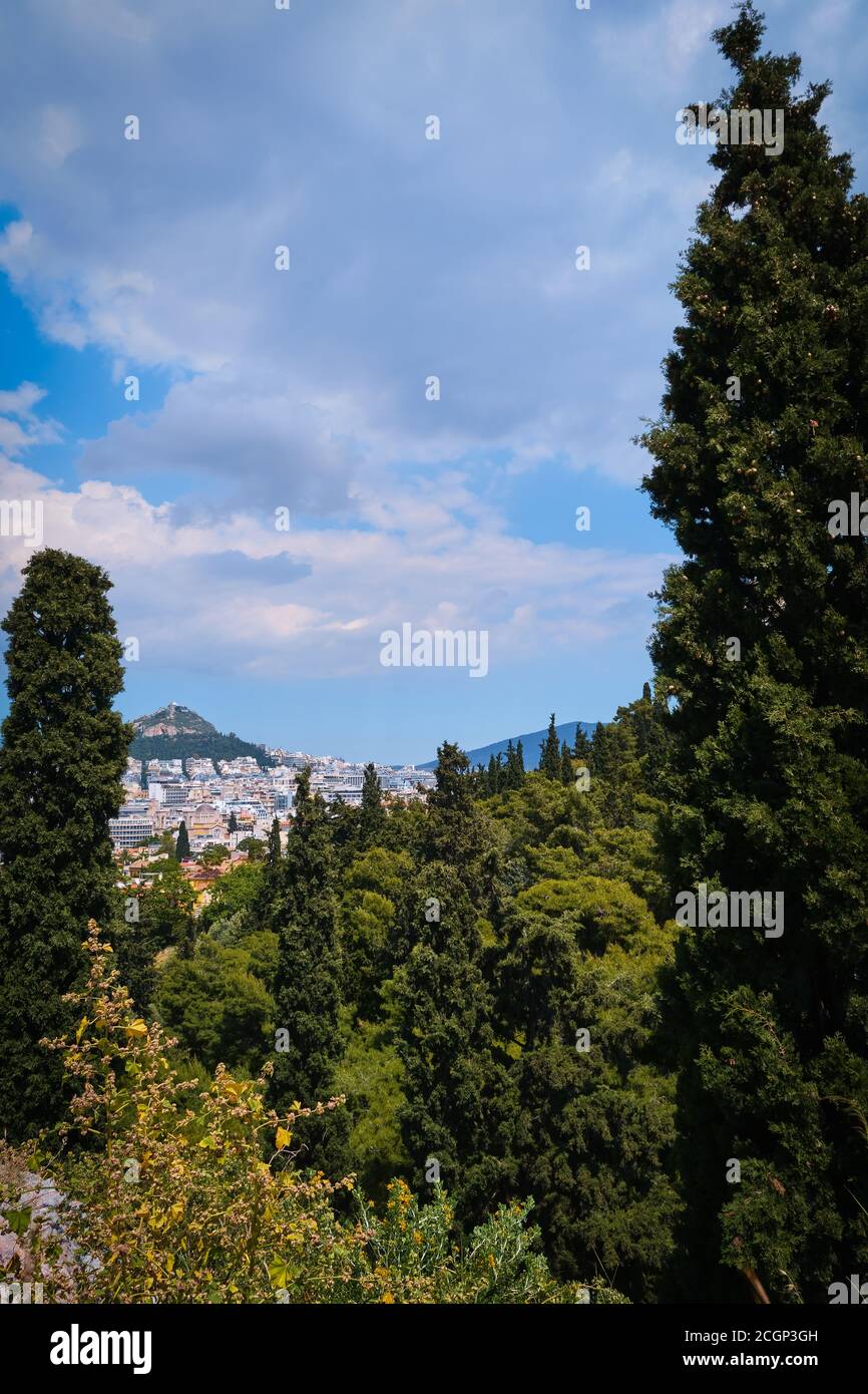 View of Lycabettus hill from Areopagus hill, rich foliage, high cedar or cypress trees. Athens, Greece. Summer day, blue sky, clouds. Selective focus Stock Photo
