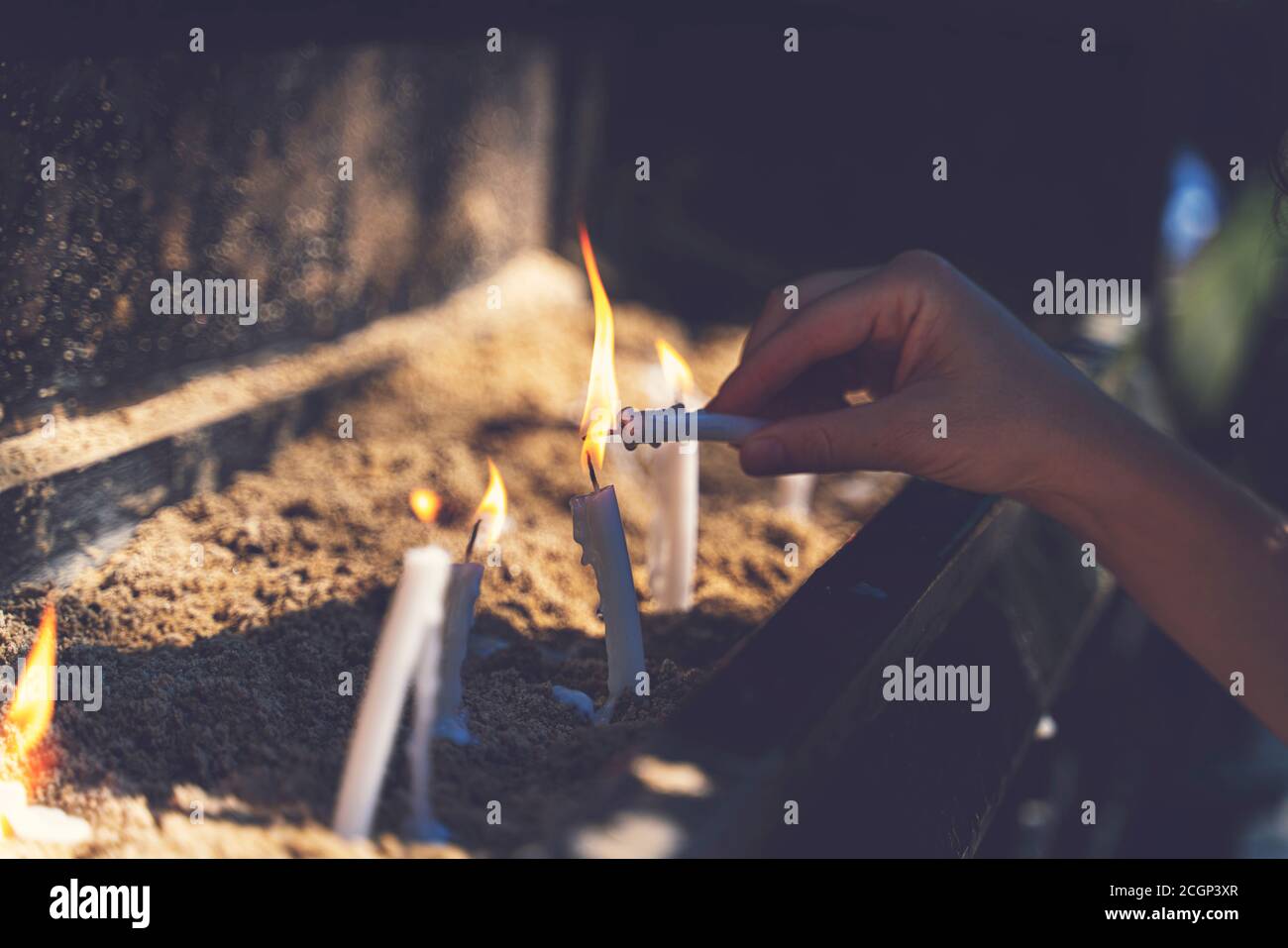 Woman praying and burning candles in the garden of the Virgin Mary house. Burning white candles on stand. Worship Stock Photo