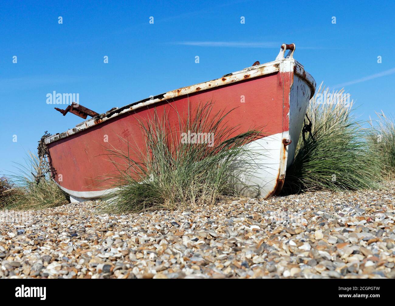 An abandoned fishing boat lies amongst the shingle and marram grass of ...