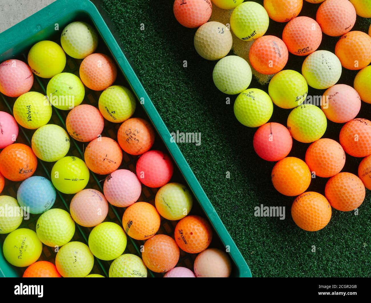 Used, coloured golf balls of assorted brands at a driving range. Stock Photo