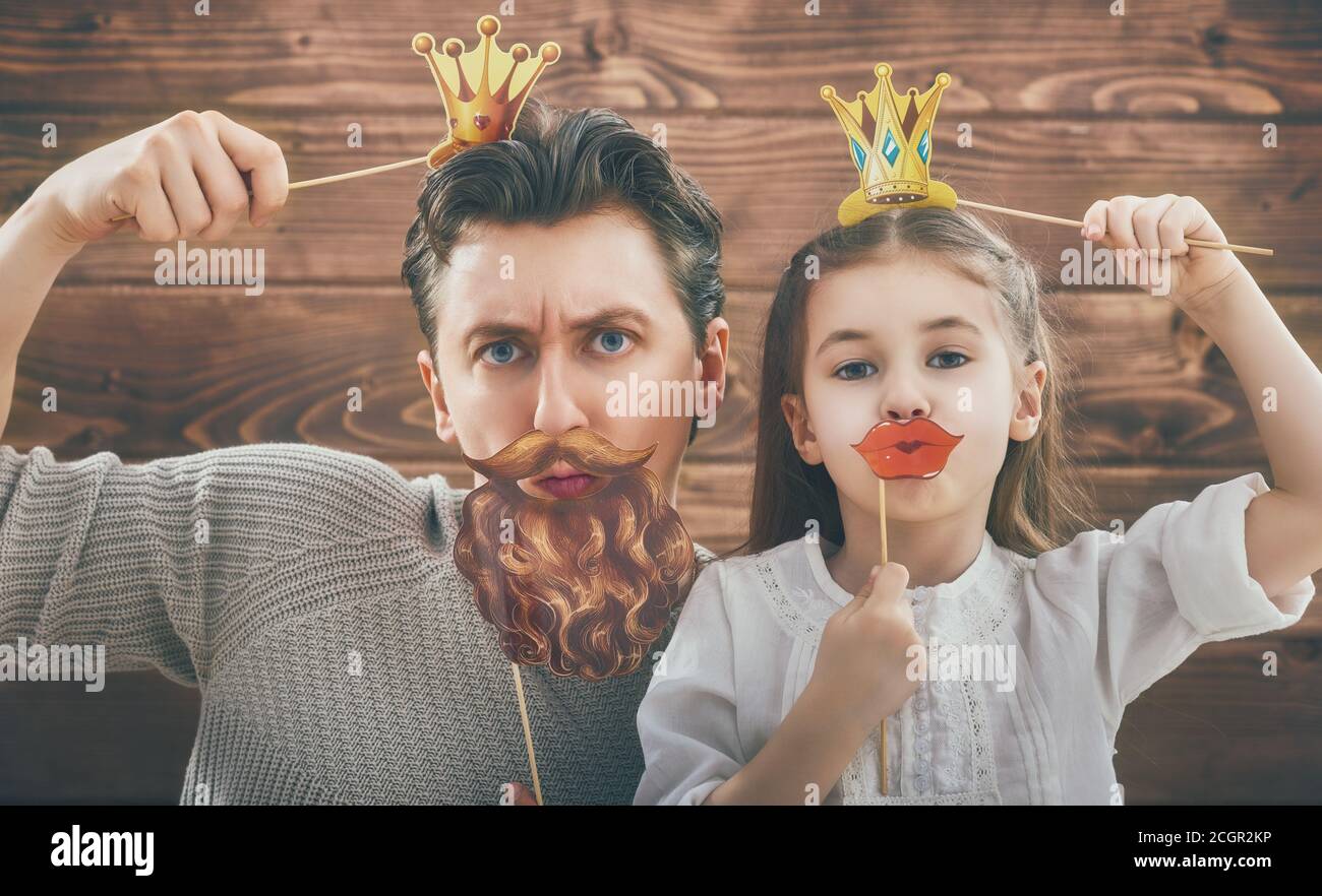 Funny family! Father and his child daughter girl with a paper accessories. Beauty funny girl holding paper lips and crown on stick. Beautiful young ma Stock Photo