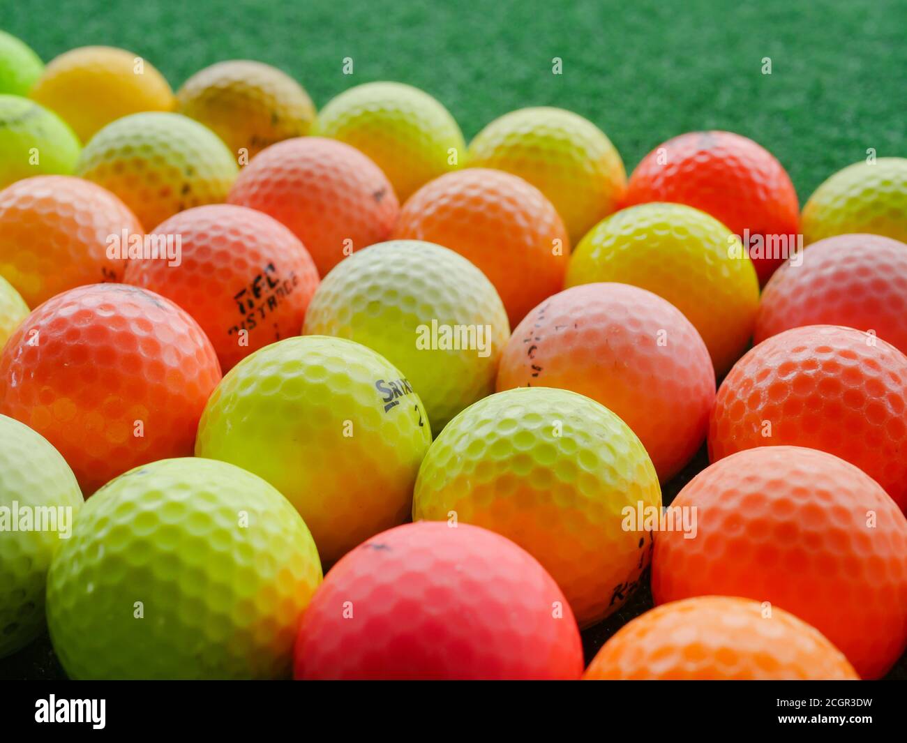 Used, coloured golf balls of assorted brands at a driving range. Stock Photo
