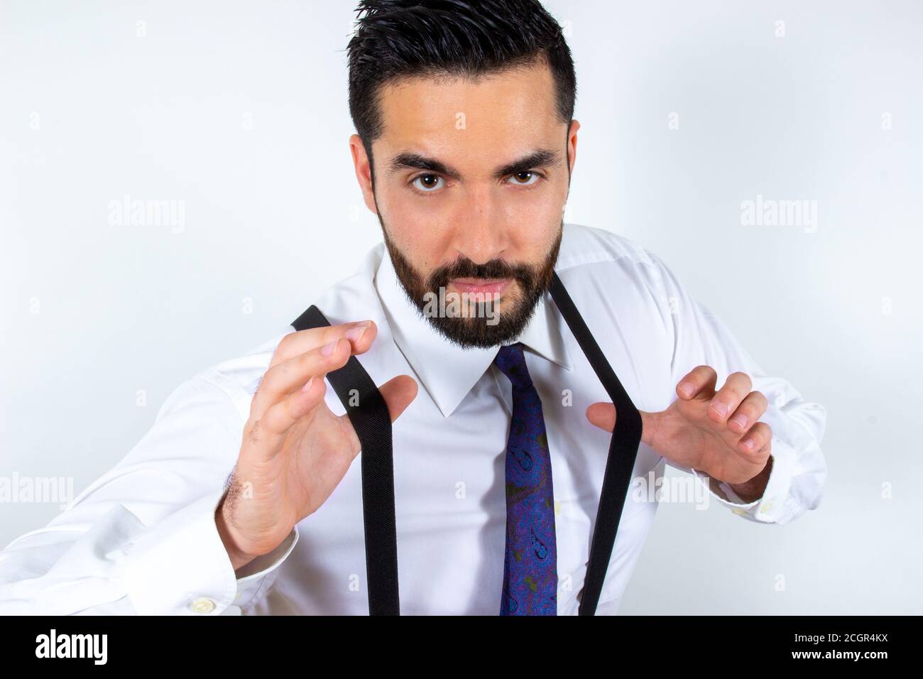Handsome young businessman pulling his suspenders, looking at camera, superiority expression. Close-up. Portrait of attractive stylish bearded man in Stock Photo