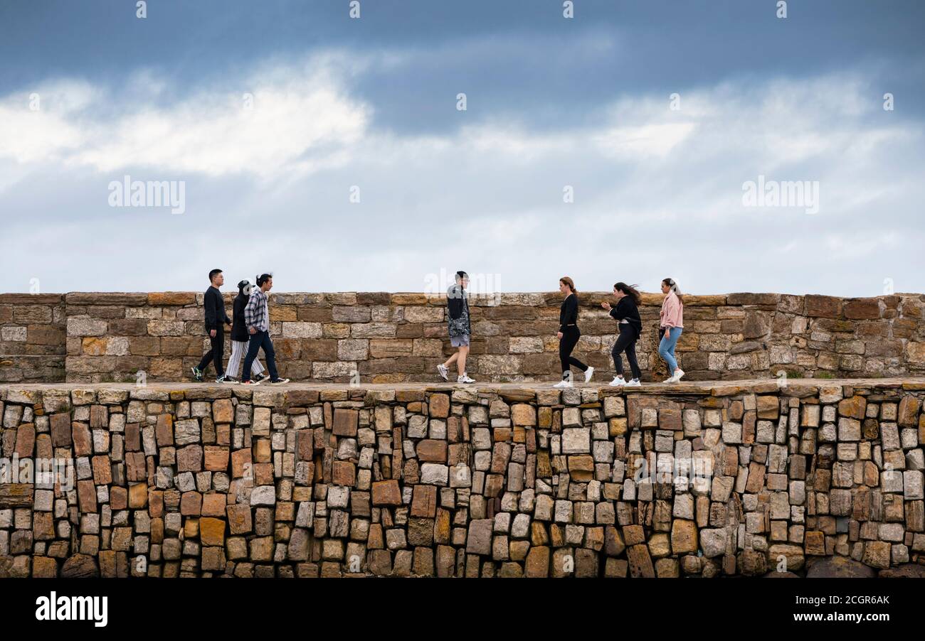 Students walking on harbour wall in St Andrews, Fife, Scotland, UK Stock Photo