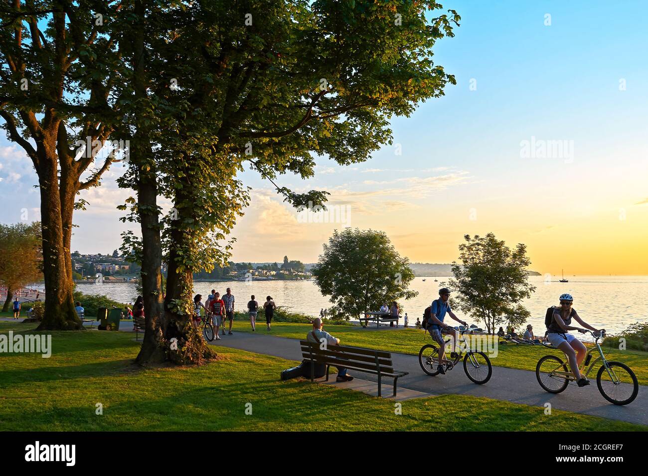 Young couple cycling, others walking or jogging late afternoon and enjoying the sunset at Stanley Park Vancouver, British Columbia, Canada Stock Photo