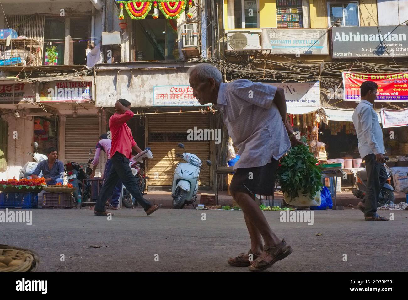 A bent old man or senior citizen is walking through Kaldadevi Road, in Bhuleshwar area, Mumbai, India Stock Photo