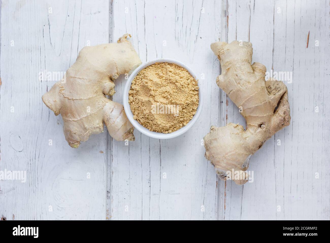 Grounded ginger and ginger root on white wooden surface. Stock Photo