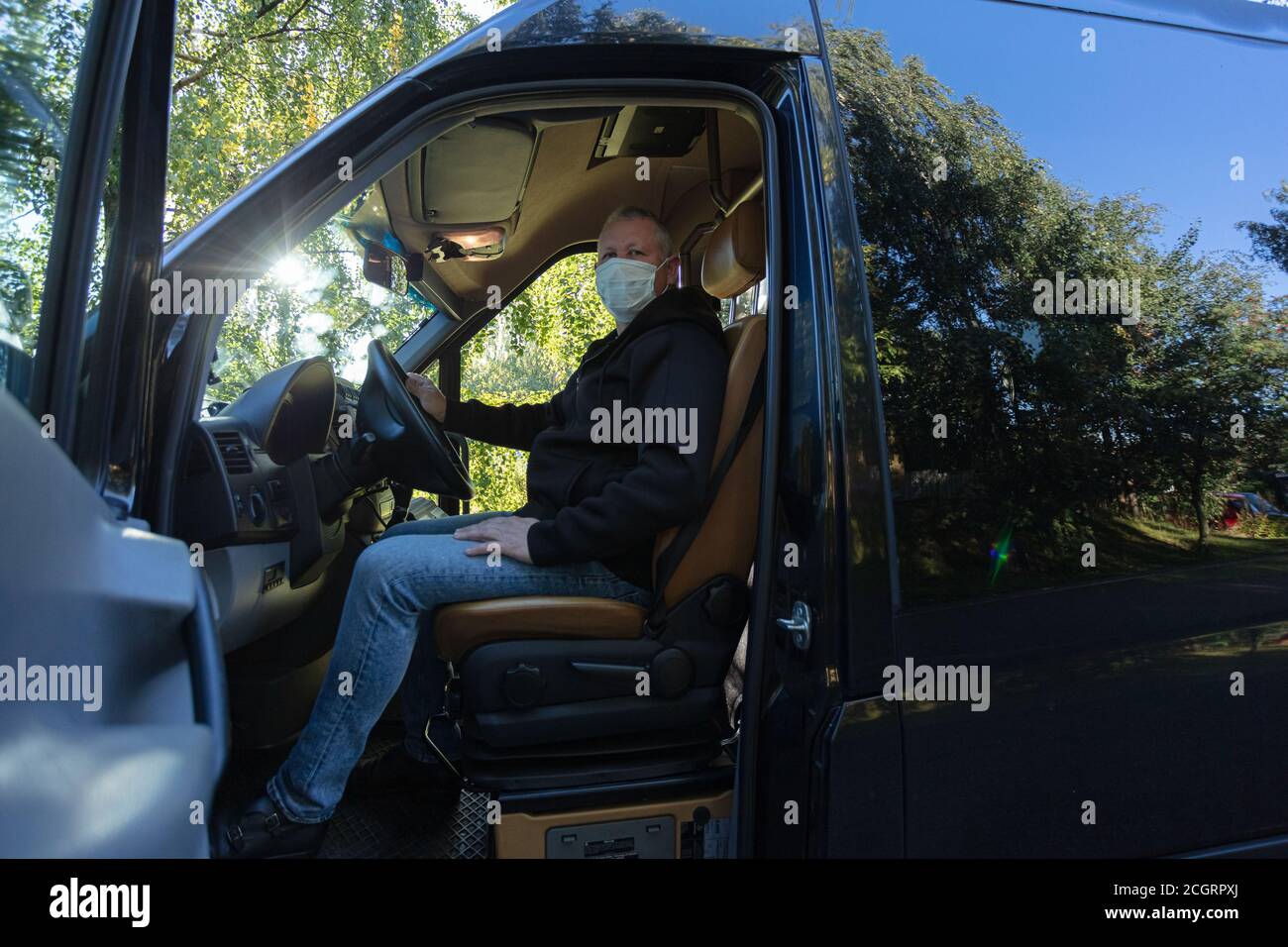 Driver in a medical mask leads a black bus Safe driving during a pandemic, protection against coronavirus. High quality photo Stock Photo