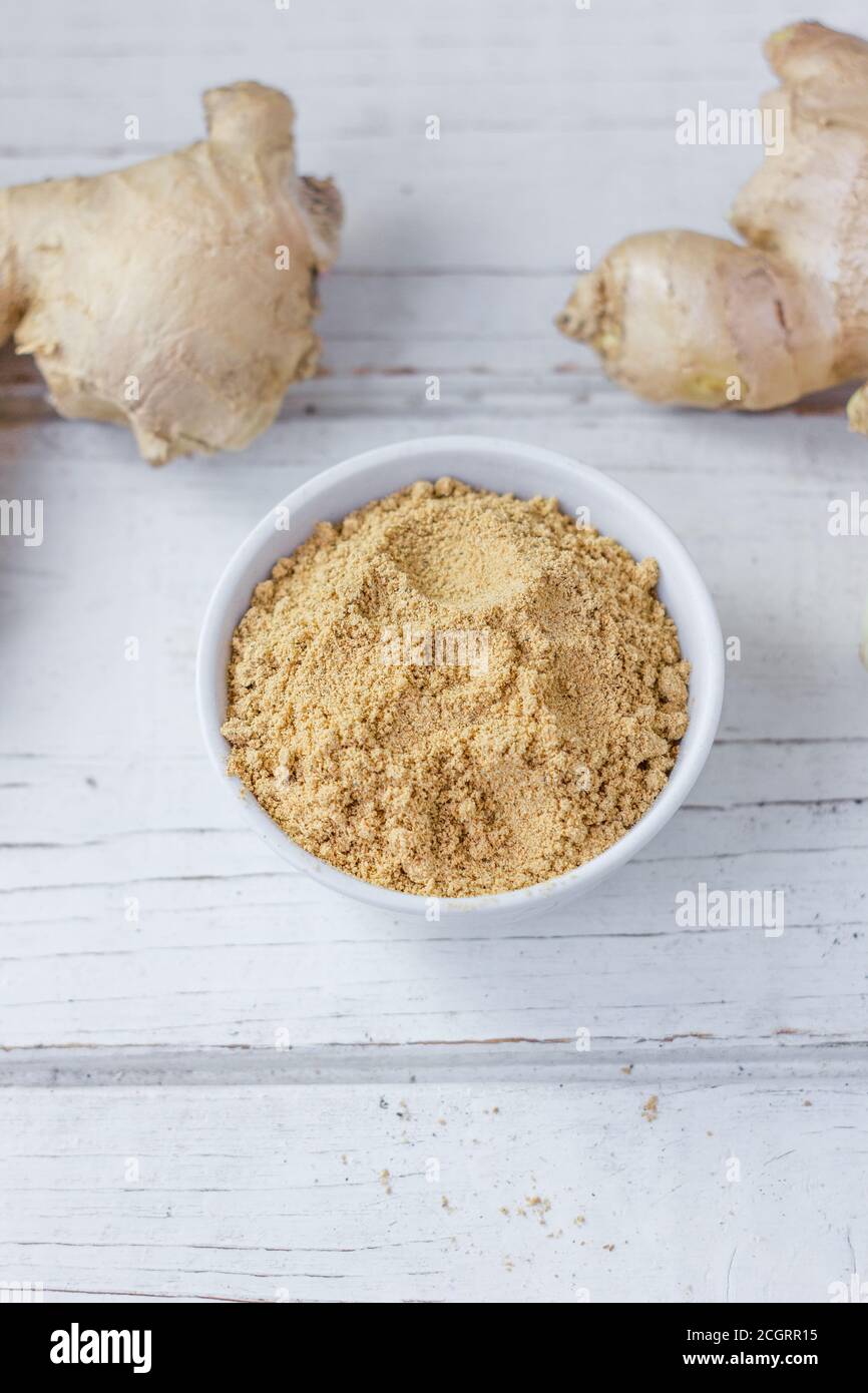 Grounded ginger and ginger root on white wooden surface. Stock Photo