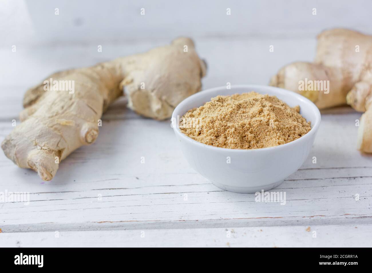 Grounded ginger and ginger root on white wooden surface. Stock Photo