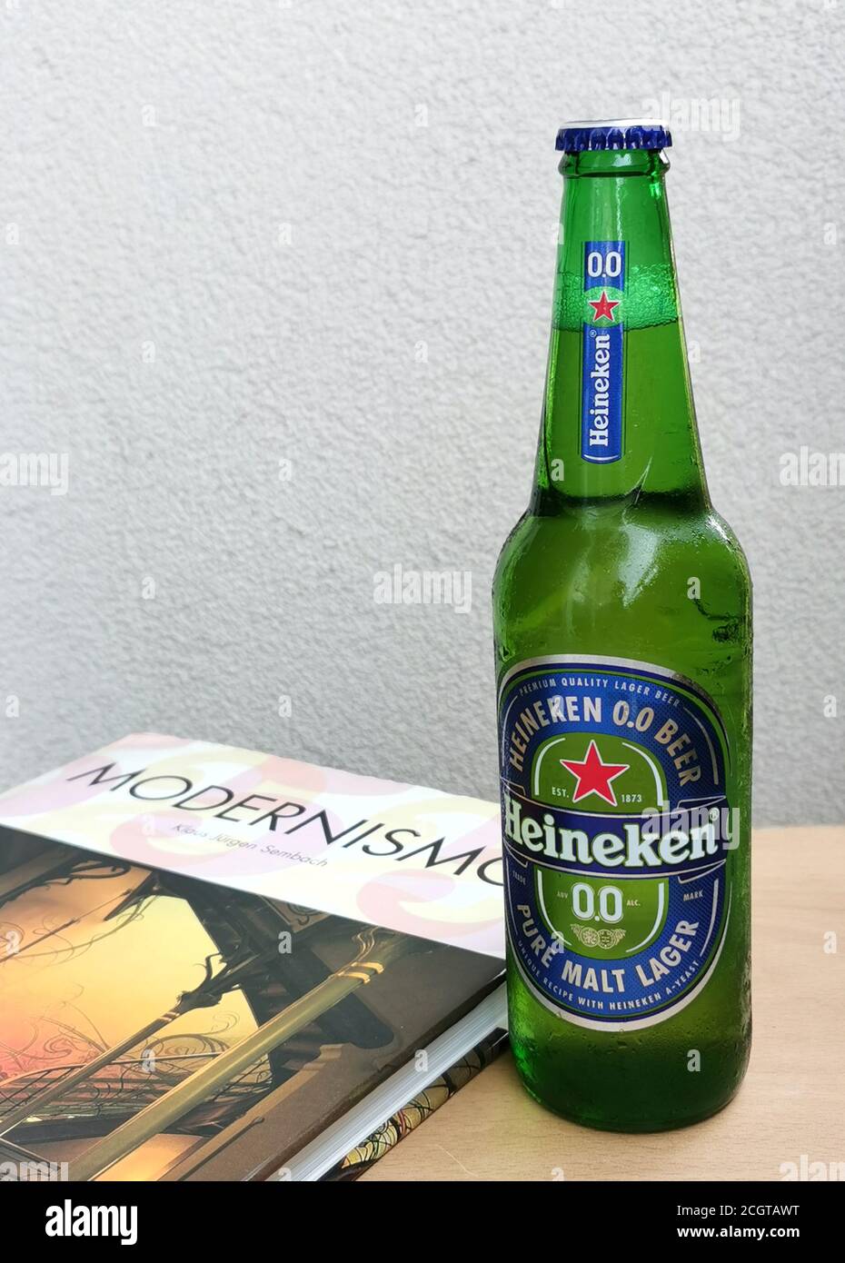 Green glass bottle of Heineken beer and book on wooden table. Stock Photo