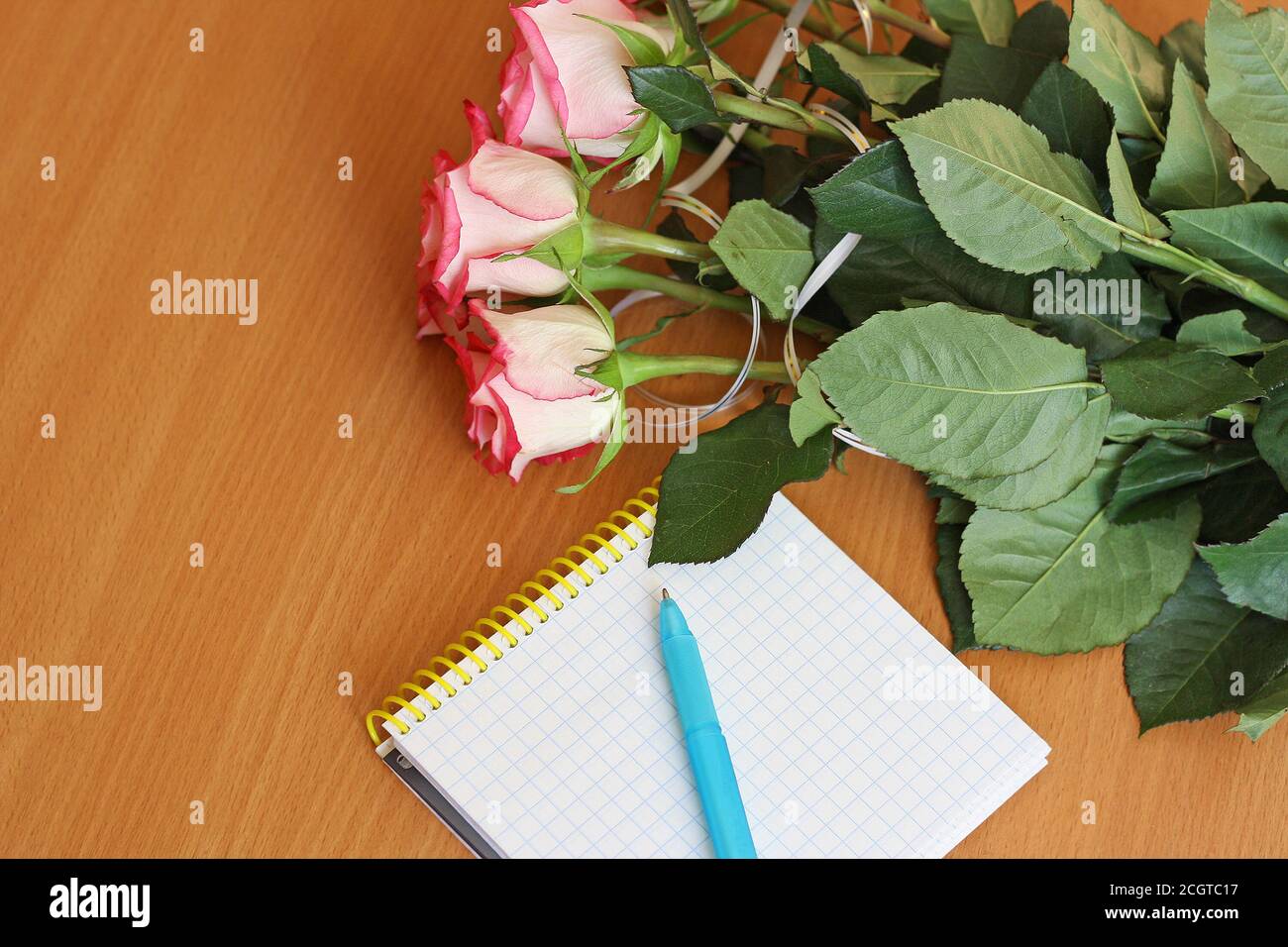 Bouquet of small pink roses, lying on the wooden surface of the table. Next to the bouquet is a notebook to record and handle. Stock Photo