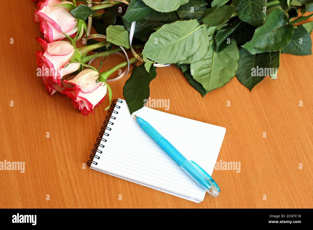 Bouquet of small pink roses, lying on the wooden surface of the table. Next to the bouquet is a notebook to record and handle. Stock Photo