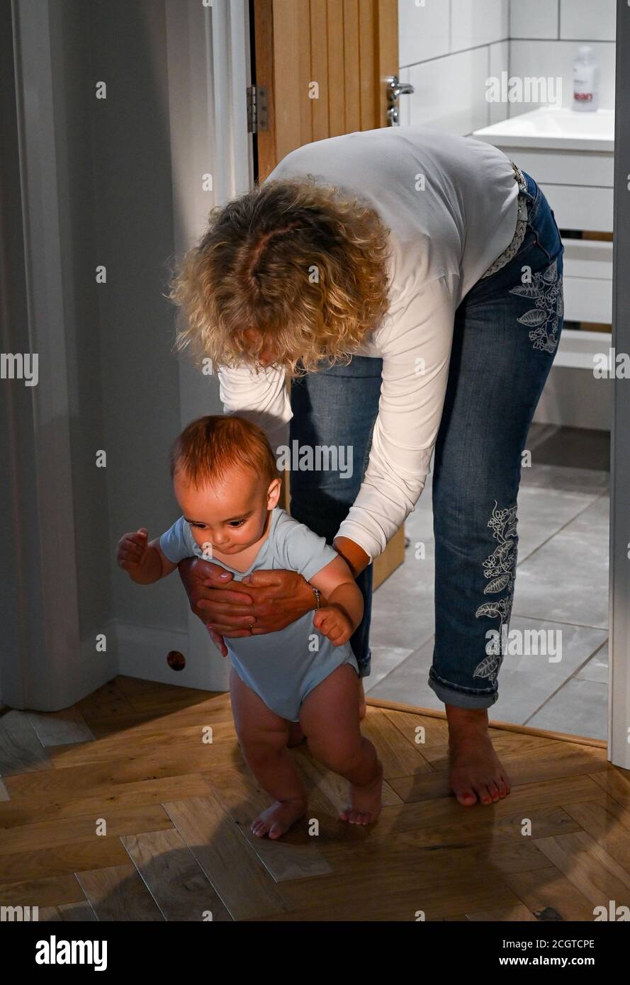 Young 10 month old baby boy learning to walk with his grandmother Stock Photo