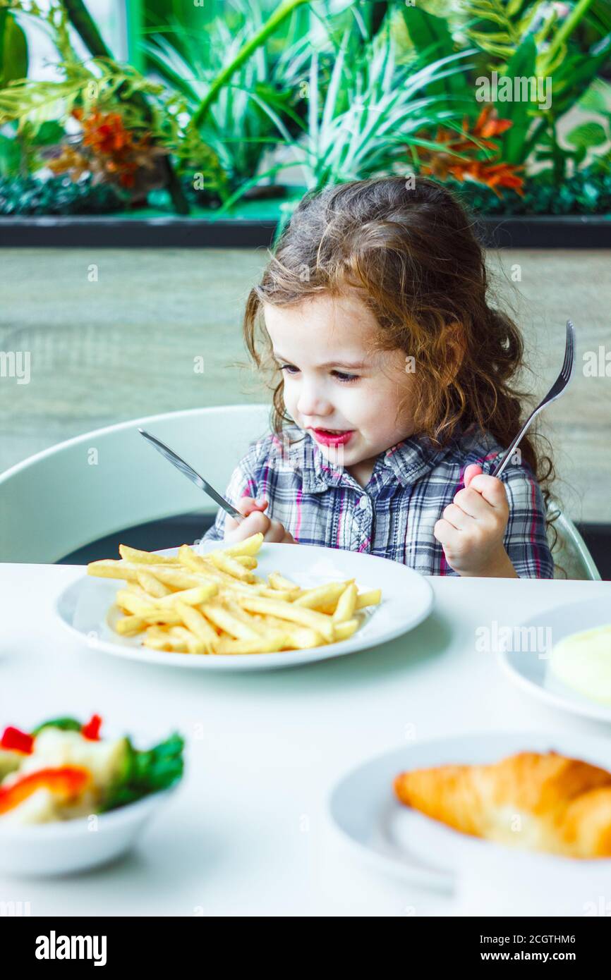 Little girl having lunch in the restaurant with the table knife and