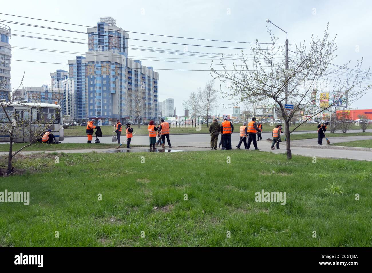 Group of cleaners of bright orange protective vests are sweeping the city sidewalk on a spring street in a residential area. Stock Photo