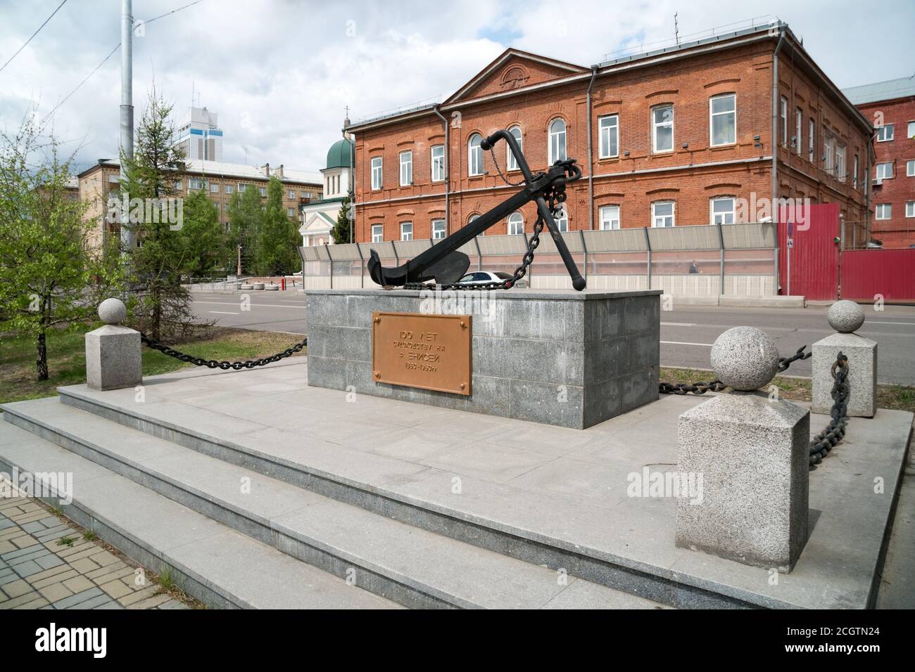 The monument in the form of an anchor in honor of the 100th anniversary of navigation on the Yenisei, against the background of the building of the Mi Stock Photo