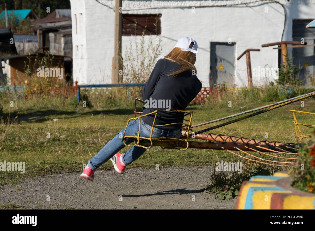 Teenager girl is spinning on a round children's swing, turned away from everyone Stock Photo