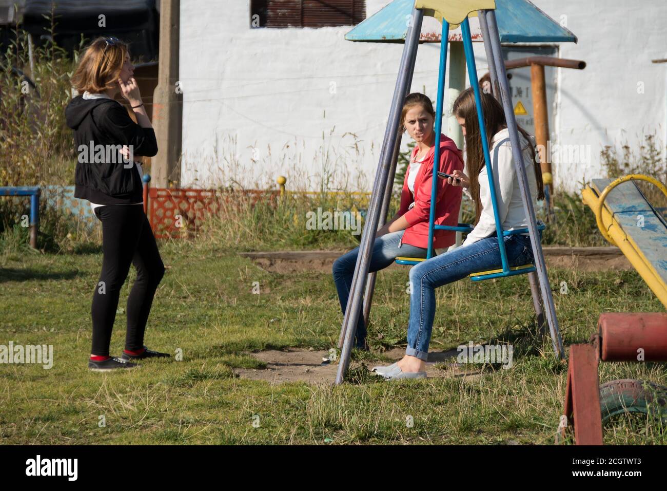 Teen girls communicate on the playground with cellphones in their hands in the courtyard of a residential building. Stock Photo