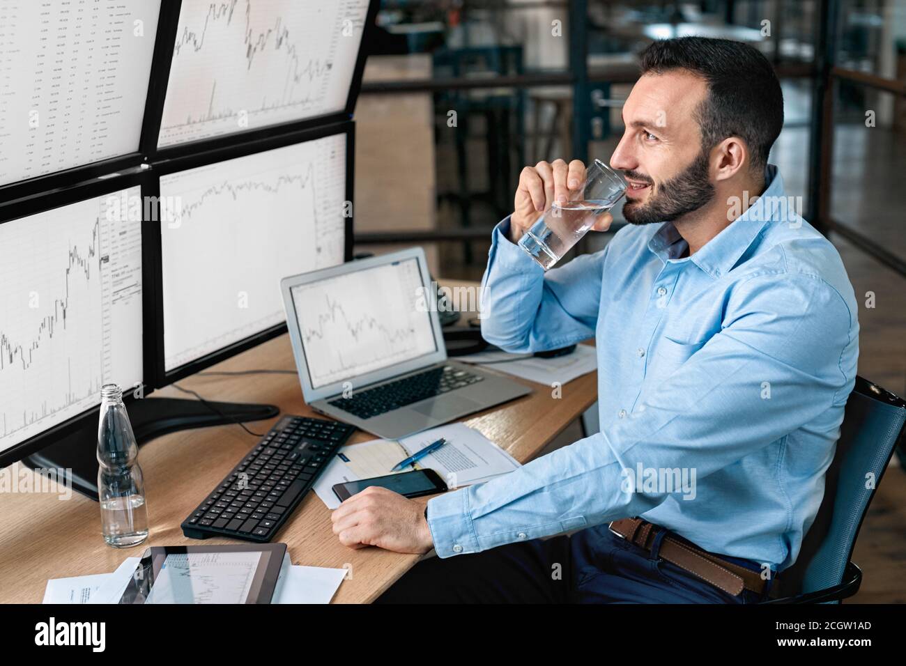 Stock Traiding. Trader sitting at office looking at monitor with chart  drinking water relaxed using trading bot to make trades cryptocurrency  exchange Stock Photo - Alamy