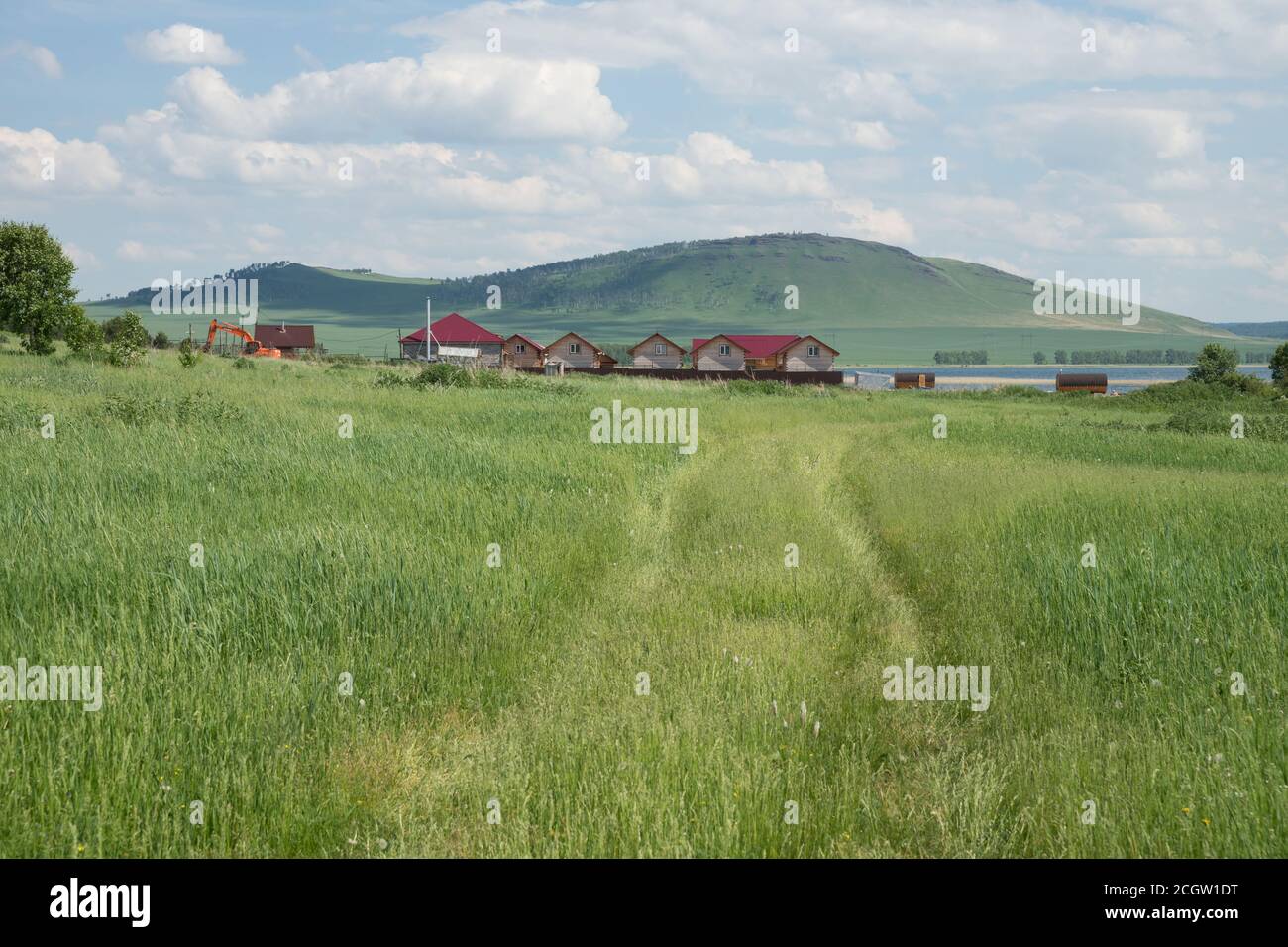 The road leads through the field to the tourist houses on the shore of the Lake Big.   Sharypovsky District of the Krasnoyarsk Territory of Russia. Stock Photo