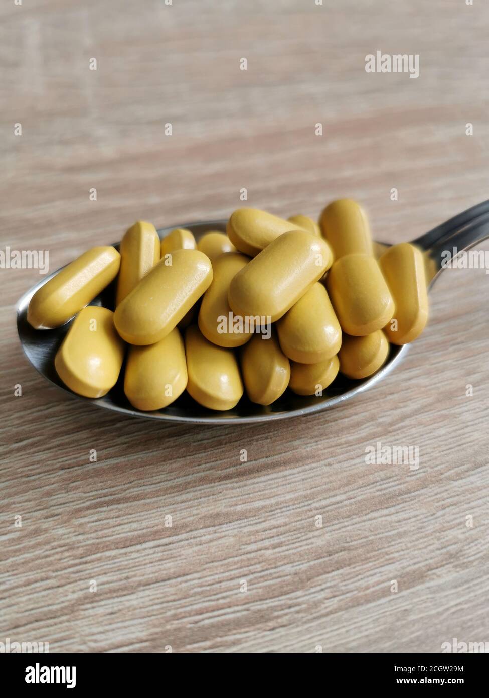 Spoon with yellow pills, dietary supplements on wooden table. Stock Photo