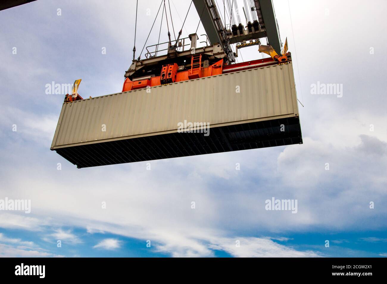 Cargo shipping container lifted by a gantry crane in a industrial shipping terminal in a port. Stock Photo