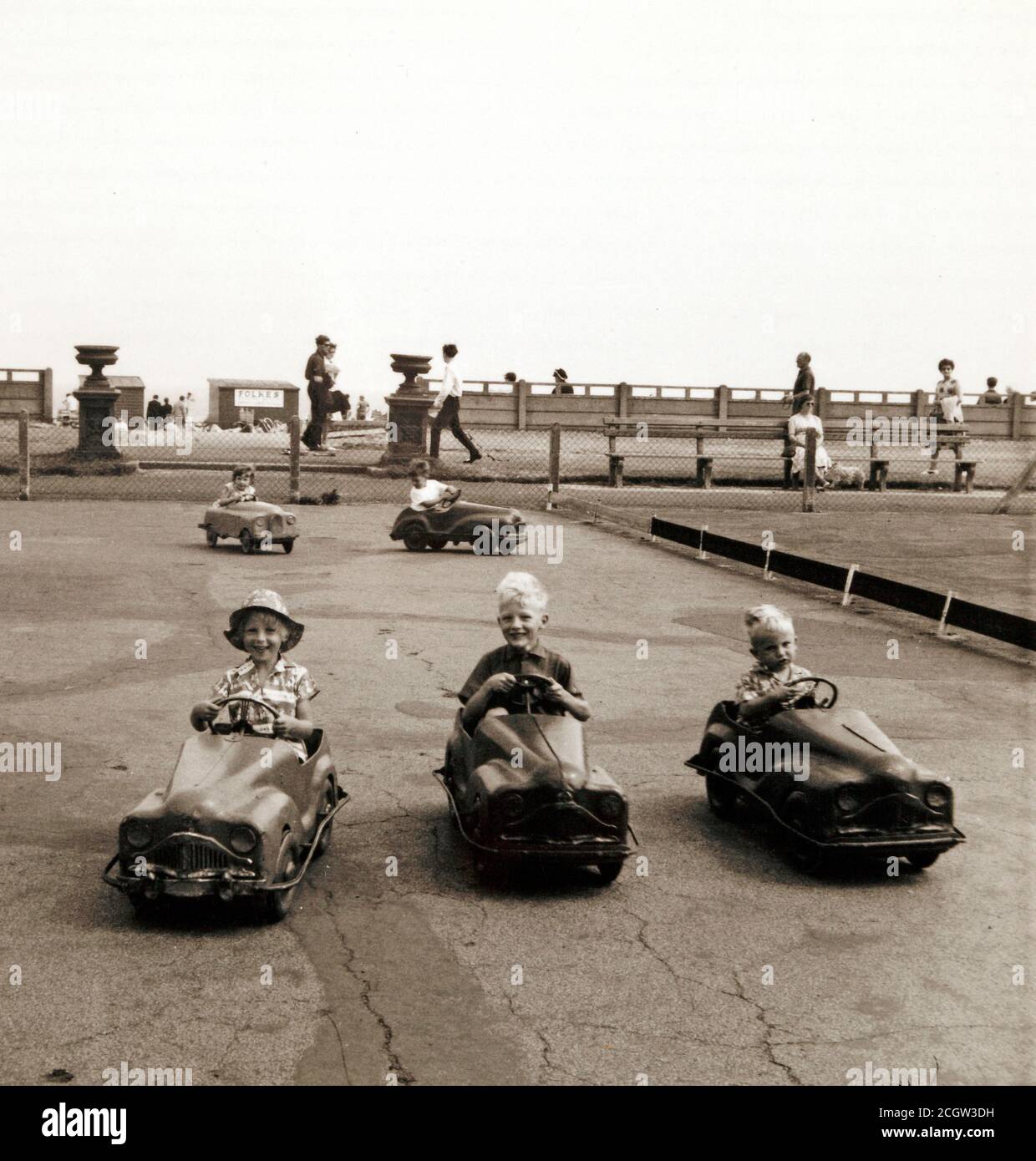 Three children in pedal cars, at a seaside amusements, 1960's. Stock Photo