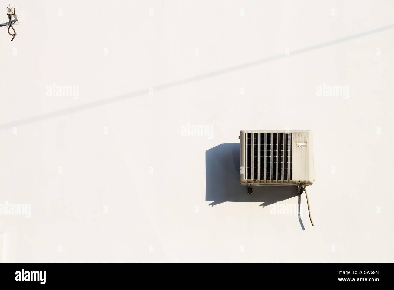 Old air conditioning machine installed on a white wall, with harsh mid day sunlight Stock Photo