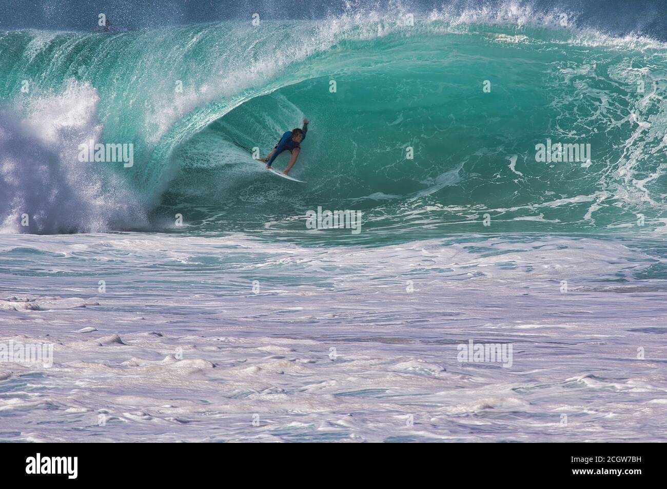 Distant view of an unrecognizable surfer in the center of a very large curl on Oahu at North shore. Stock Photo