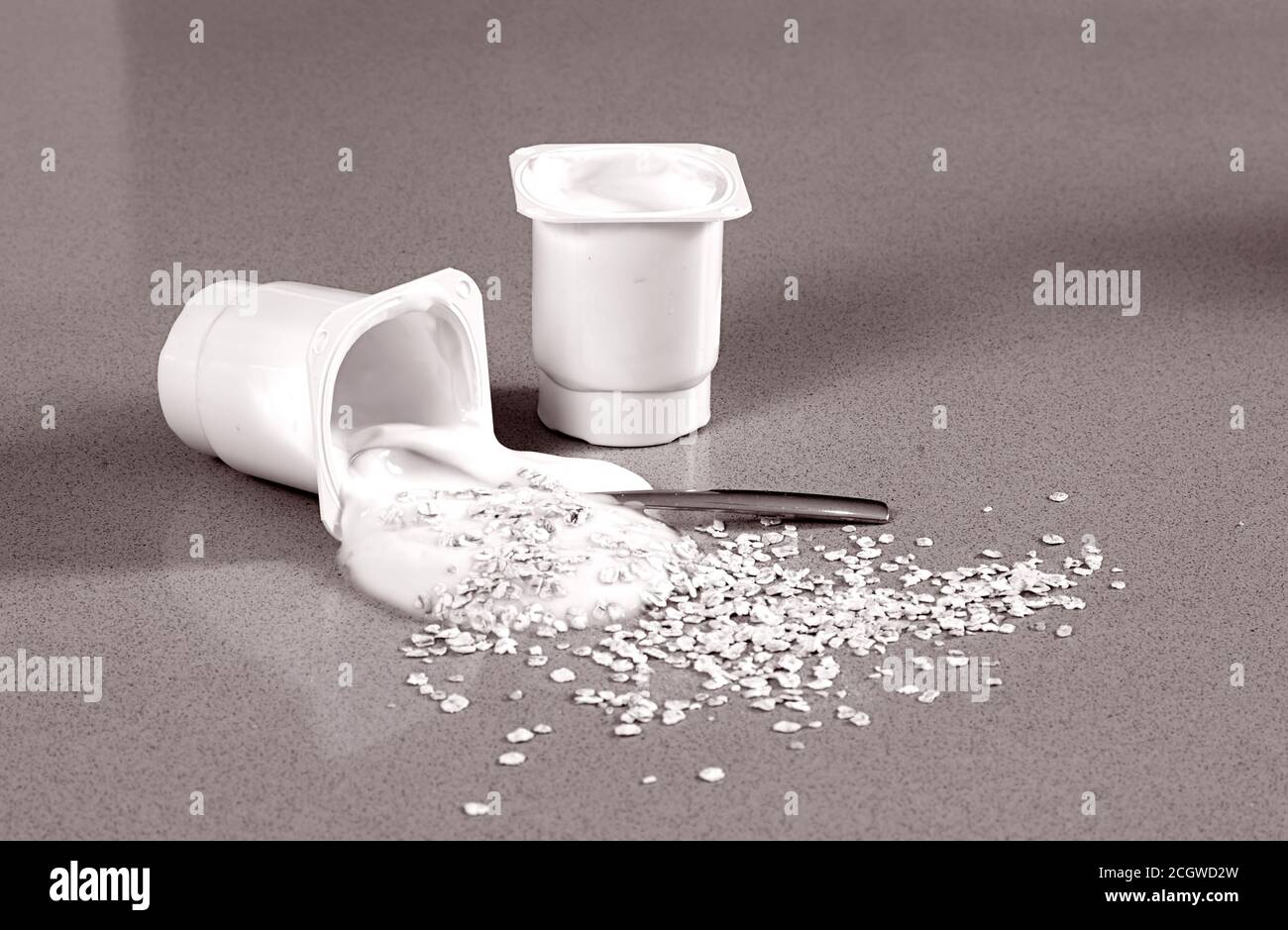 Cup of yoghurt with cereals someone has left spilt on the table Stock Photo