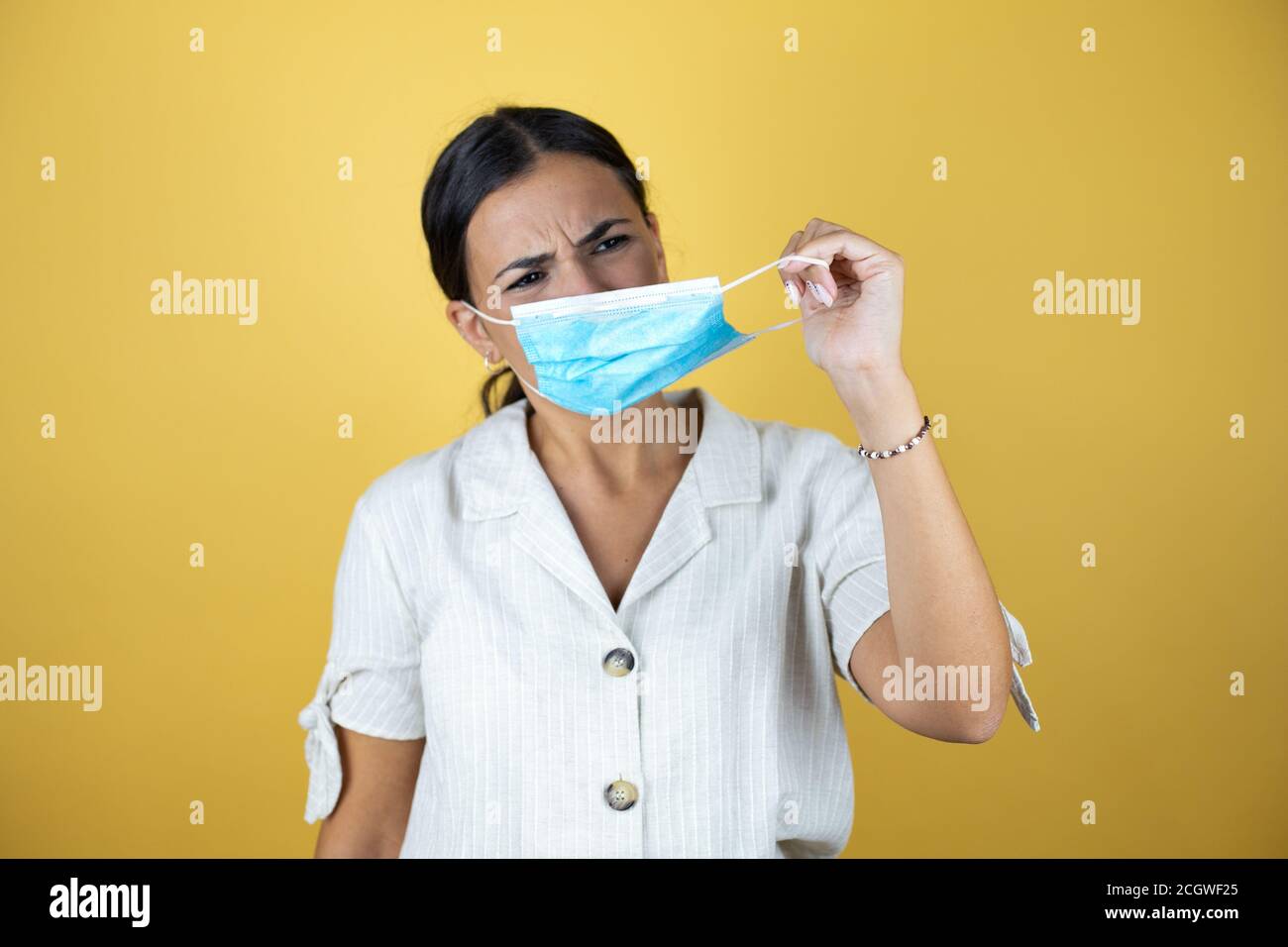 Beautiful woman over yellow background taking off the medical mask ...