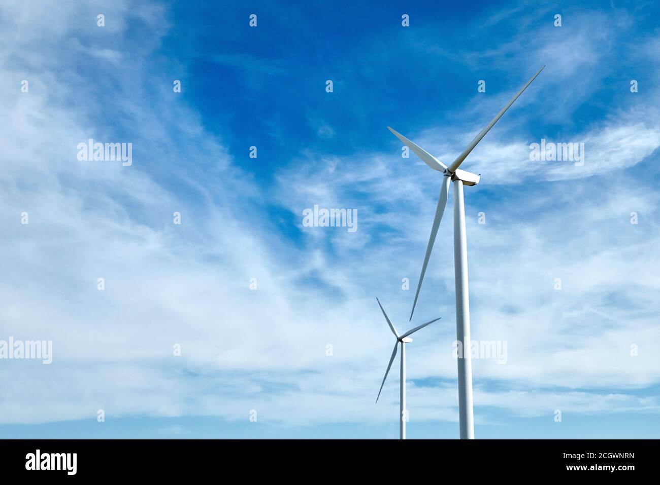 Two wind power turbines against a blue sky with white clouds. Renewable ...