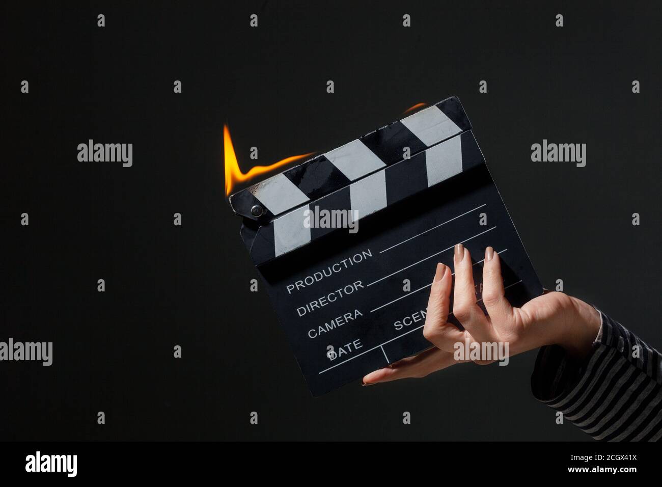 Female hand holding clapperboard on fire. Burning flames from a movie clap board. Stock Photo