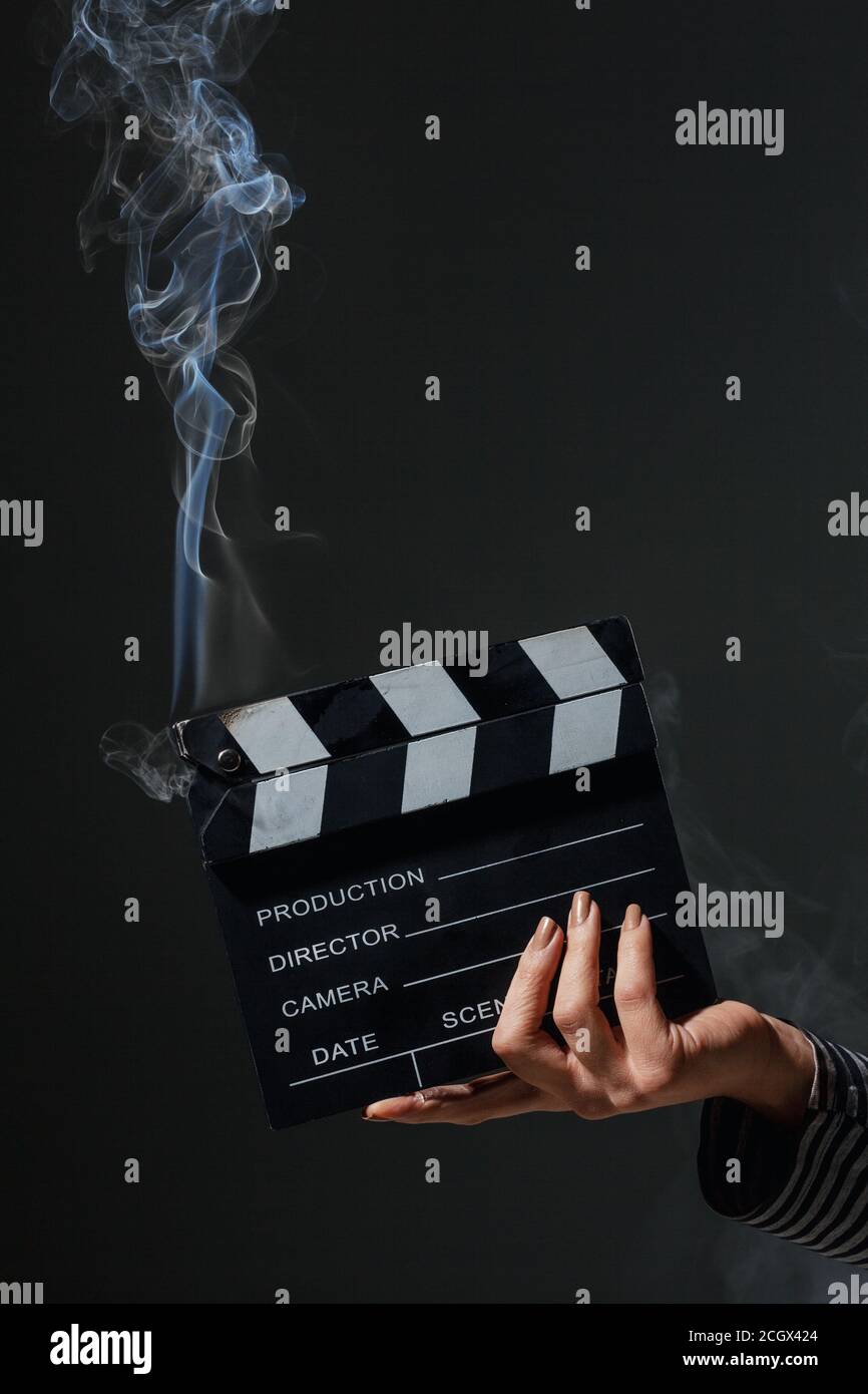Female hand holding smoking clapperboard. Smoke comes out of hot movie clap board. Stock Photo