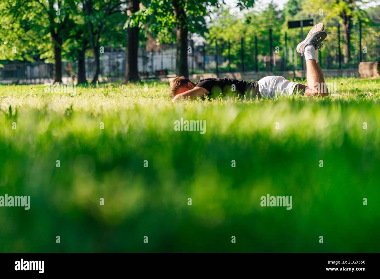 Athletic sportsman laying on the green grass and resting from a workout in the park Stock Photo