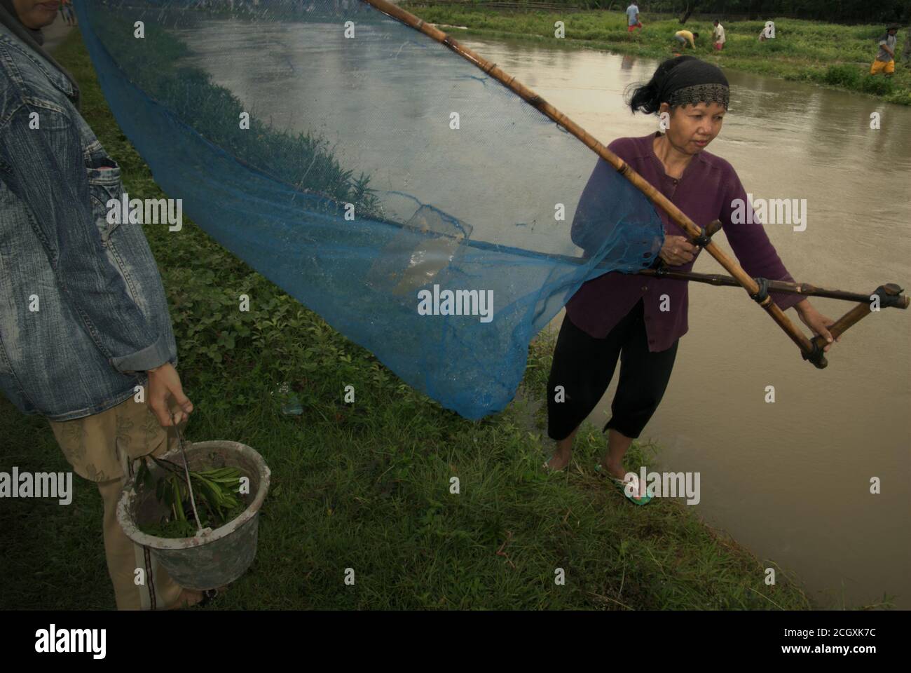 A woman handling a pushnet as she stands on the bank of an irrigation canal in Karawang regency, West Java province, Indonesia. Stock Photo