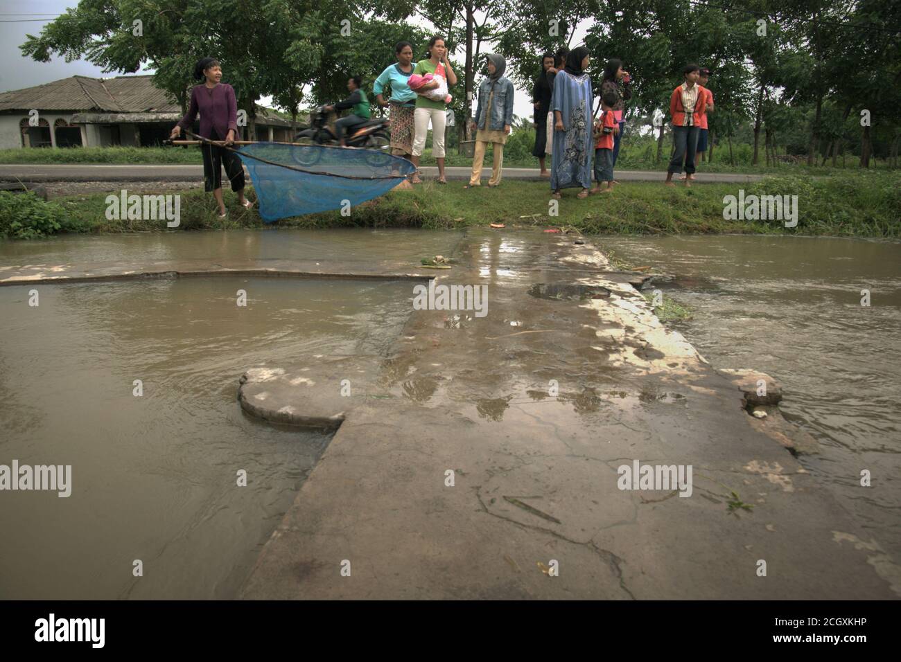 A woman holding a pushnet as people gathers on the bank of an irrigation canal in Karawang regency, West Java province, Indonesia. Stock Photo