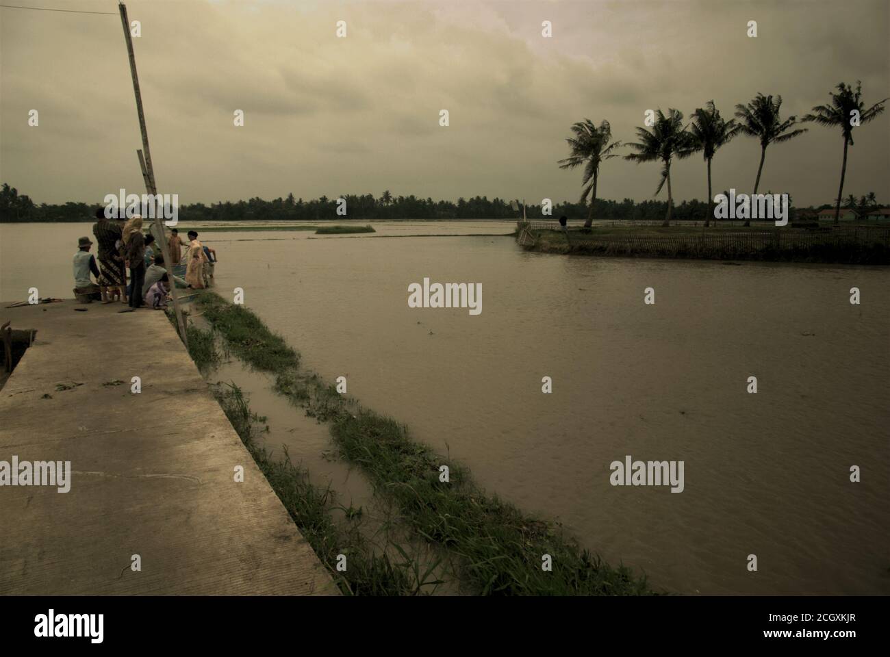 Farmers grouping on a concreted walking path to fish, as torrential rains during rainy season have left some agricultural areas flooded in Karawang regency, West Java province, Indonesia. Stock Photo